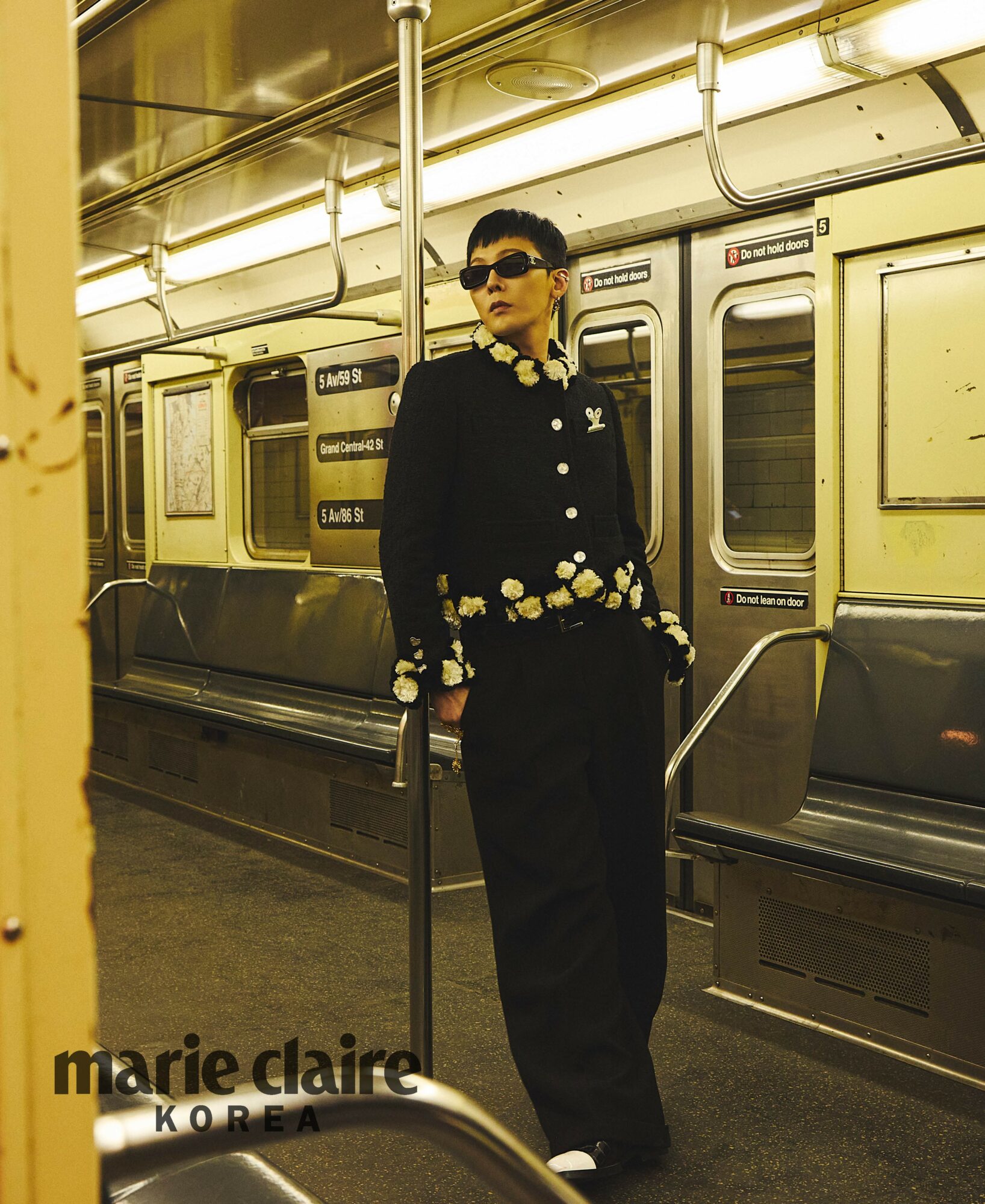 Person standing inside subway train, wearing sunglasses and a dark outfit with decorative buttons, holding a cane.