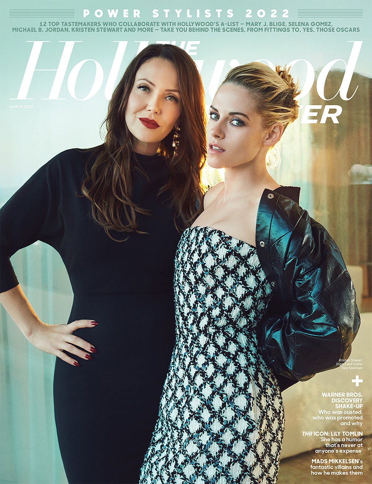 Two women pose indoors, one with long dark hair in a black outfit, the other with blonde hair in a patterned dress and leather jacket.