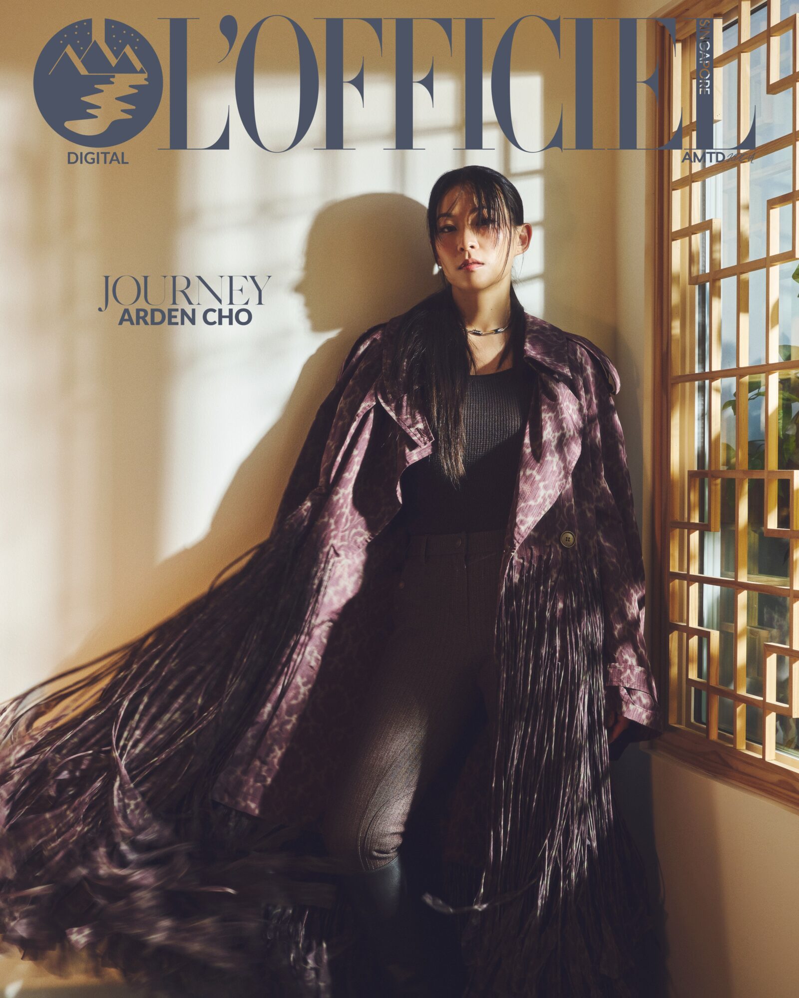 Woman with long dark hair in a shiny purple coat standing by a window with wooden lattice, sunlight casting shadows.