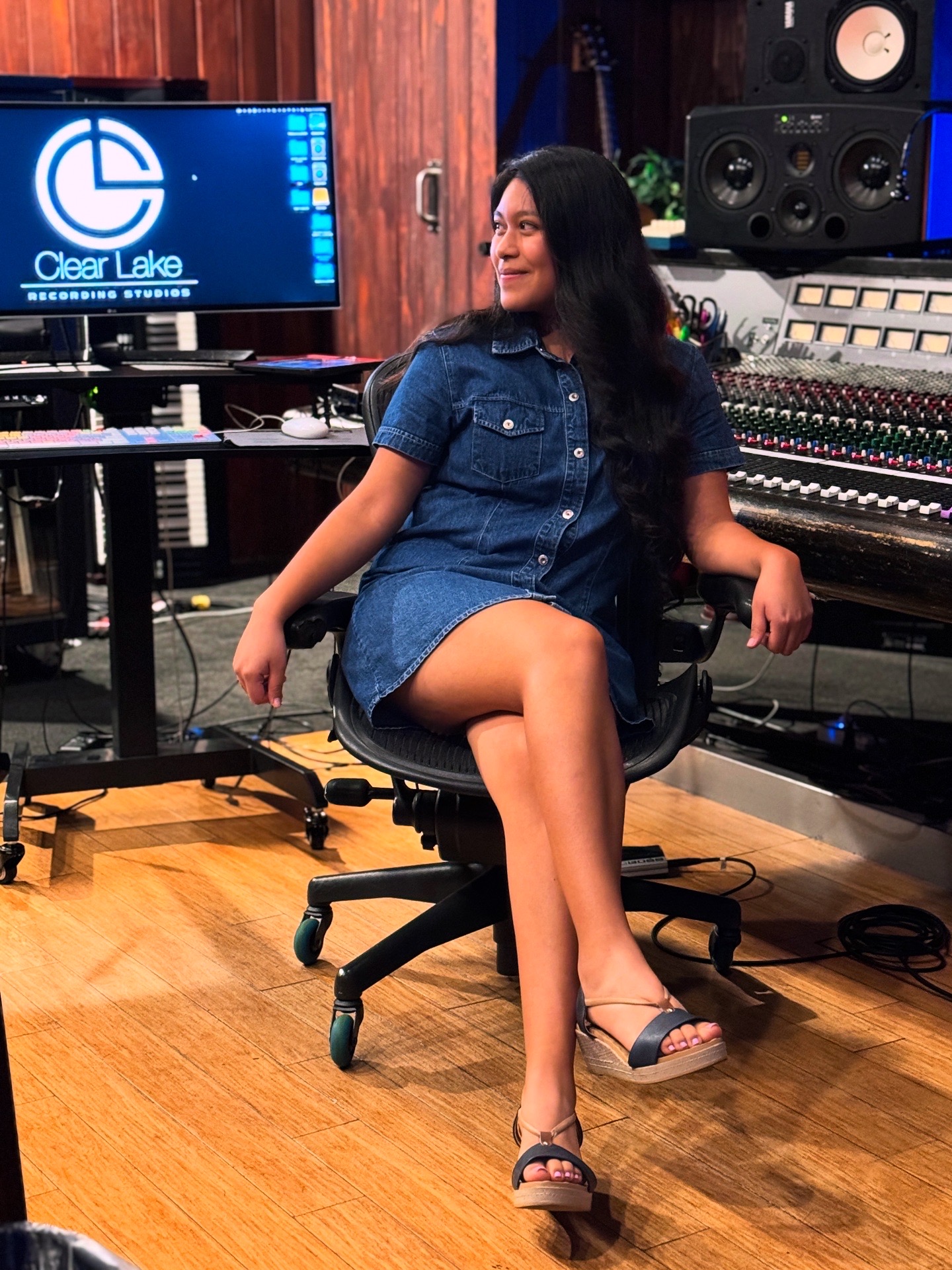 Woman sitting in a recording studio with music equipment and a monitor displaying 'Clear Lake'.