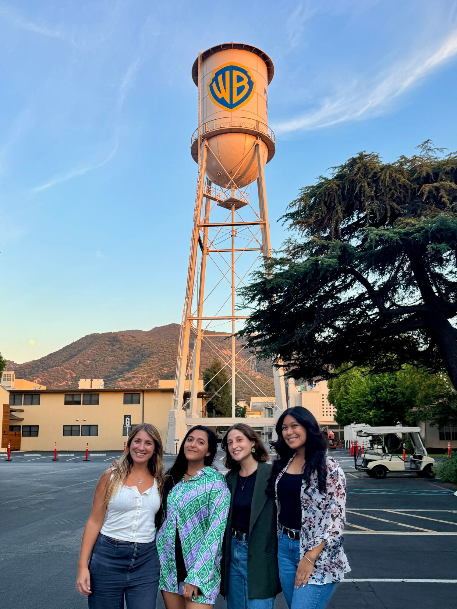 Four women standing in parking lot with water tower and trees in background.