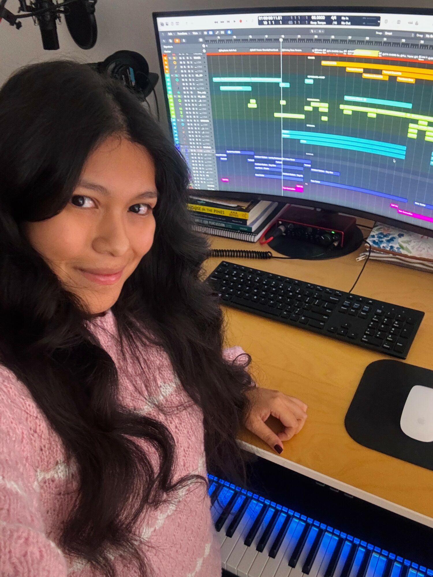 Young woman with long dark hair taking a selfie in front of a computer with music production software open.