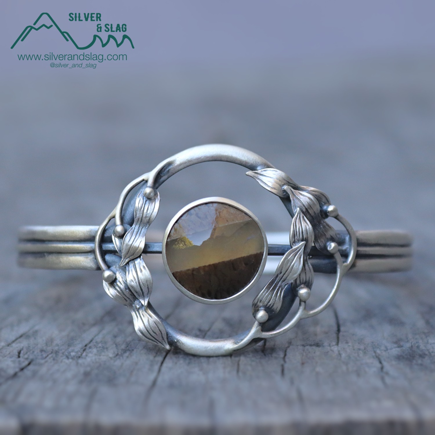 Silver bracelet with circular mirror and decorative wire design, placed on a wooden surface.