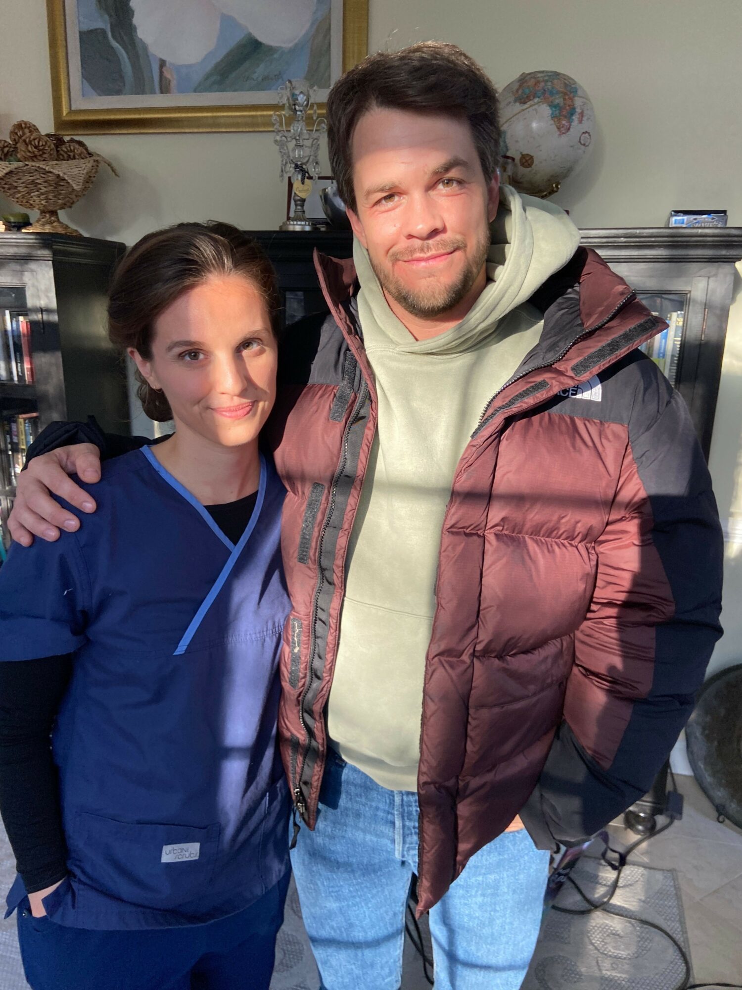 Two people standing close together indoors, smiling, with a fireplace and decorative items in the background.