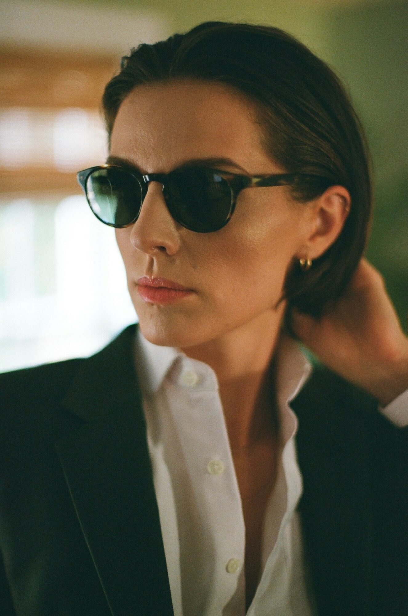 Woman with dark hair wearing sunglasses and a white shirt, looking to the side indoors.