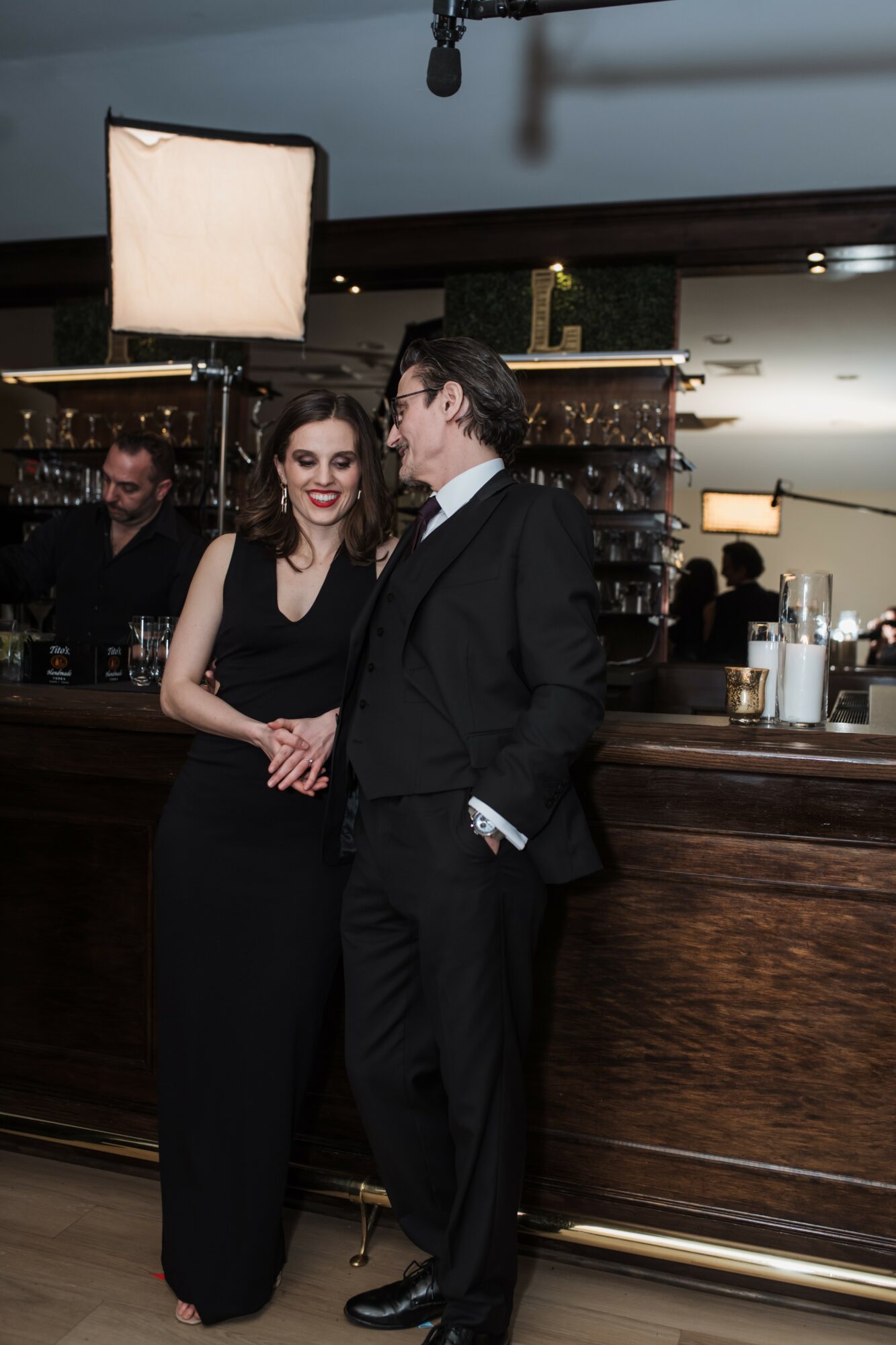 Man and woman in formal attire talking at a bar in a dimly lit setting.