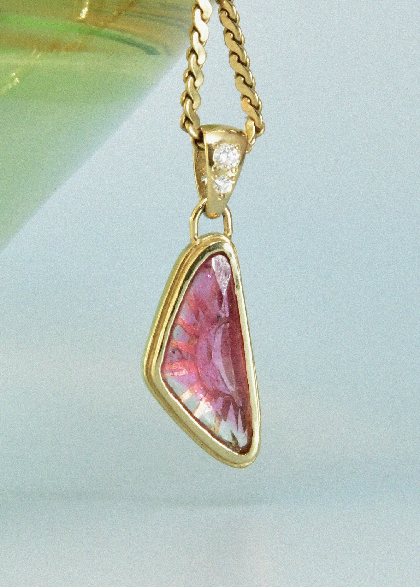 Gold chain necklace with a pink and white irregular-shaped pendant hanging against a light background.