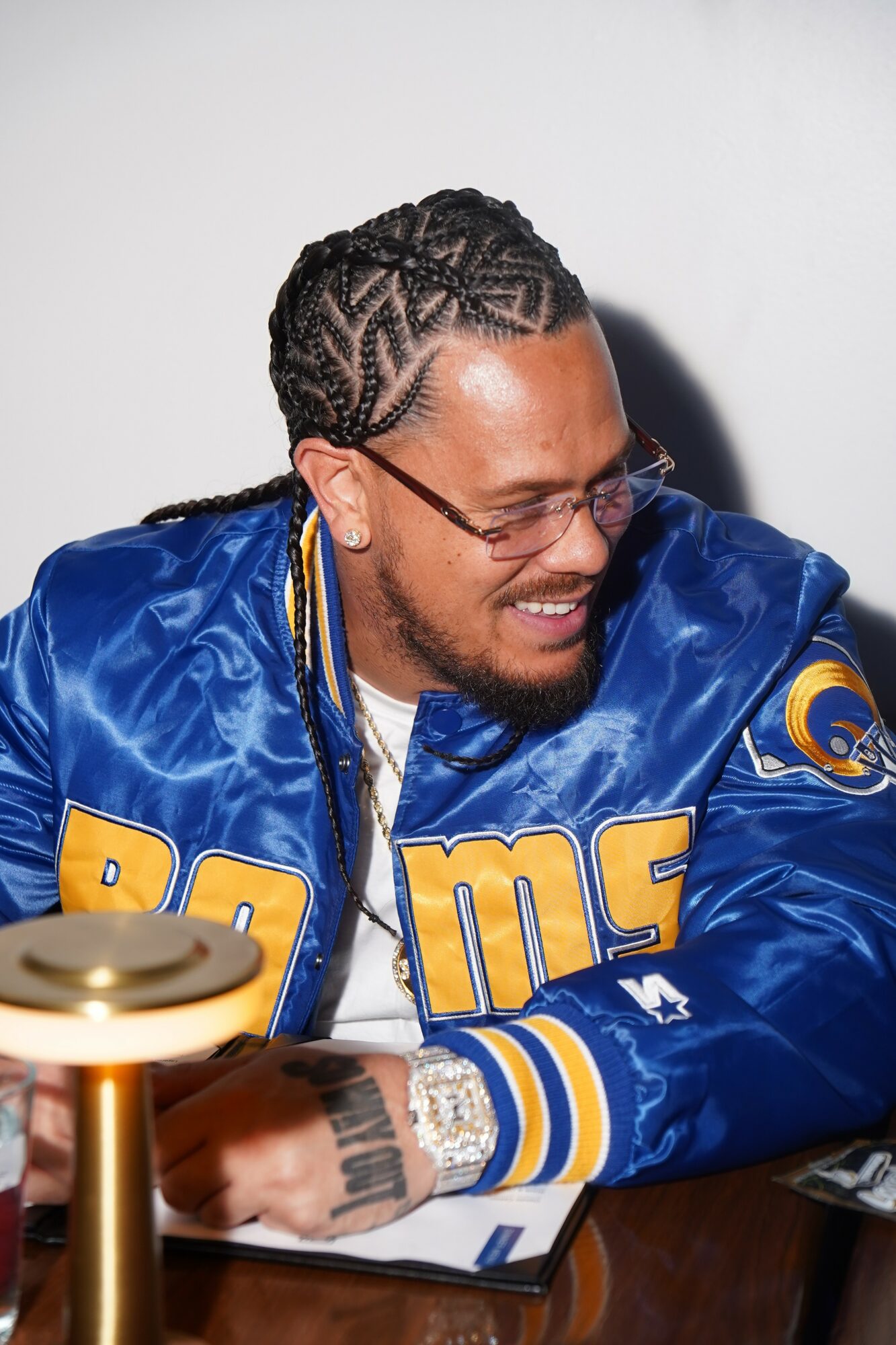 Person with braided hair, glasses, and a blue sports jacket smiling and looking down.