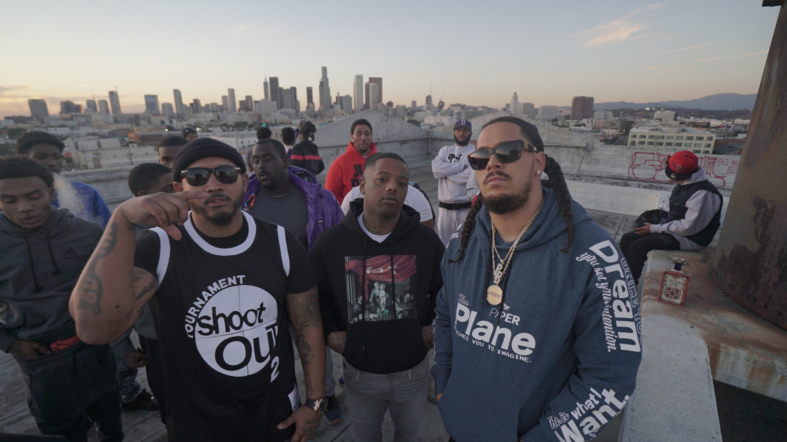Group of people on rooftop with city skyline in background, some wearing sunglasses and casual clothing.