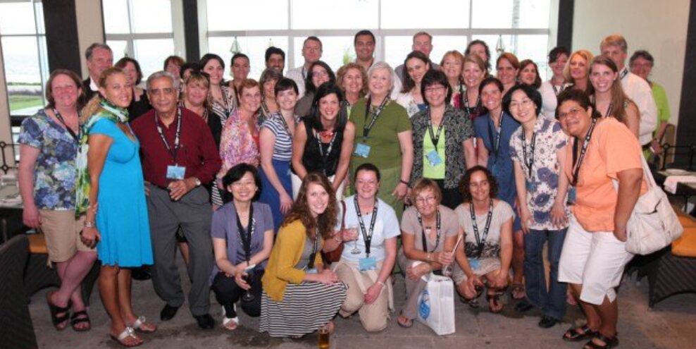 Group of diverse people gathered indoors, posing for a photo, with large windows in the background.