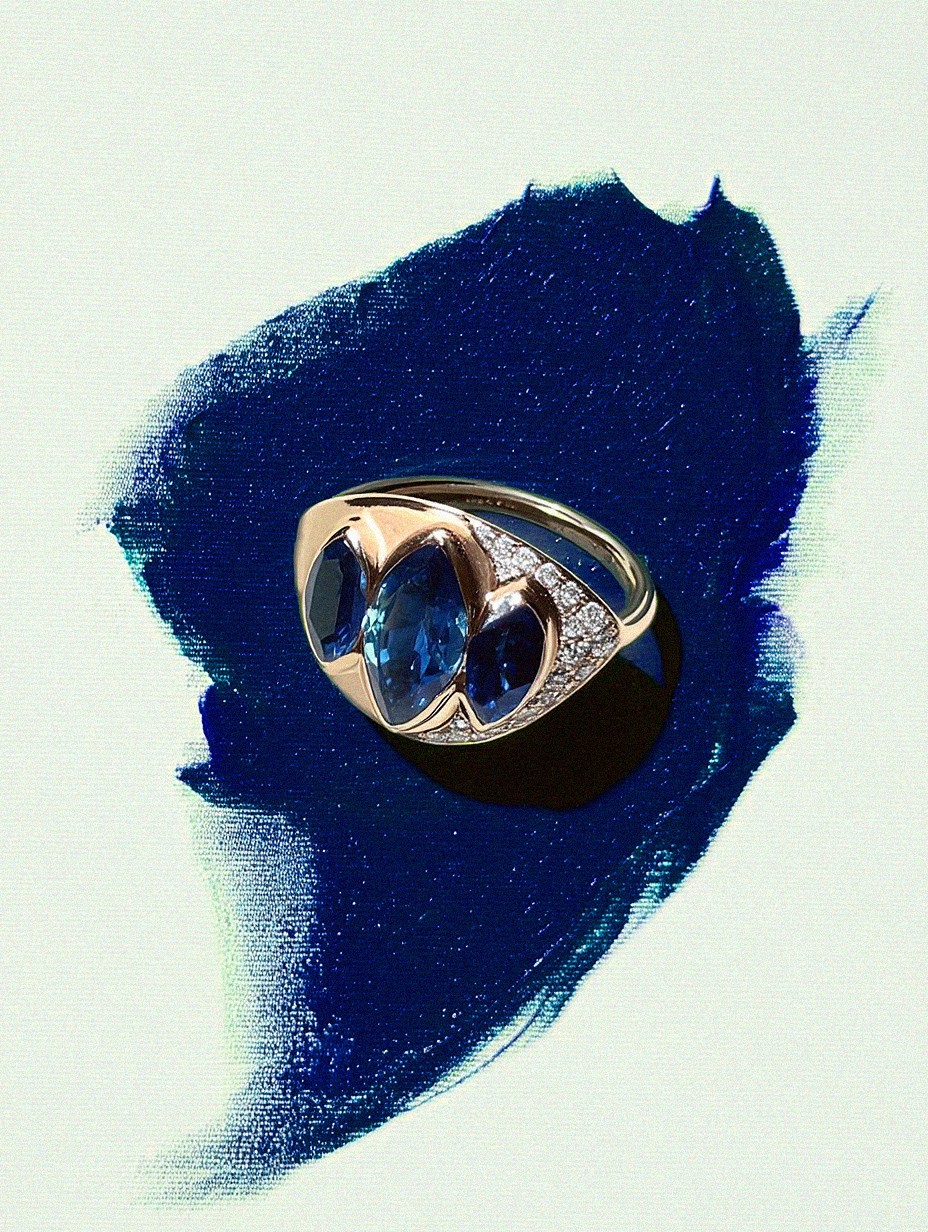 Ring with blue gemstone and diamond accents on a blue and white abstract background.