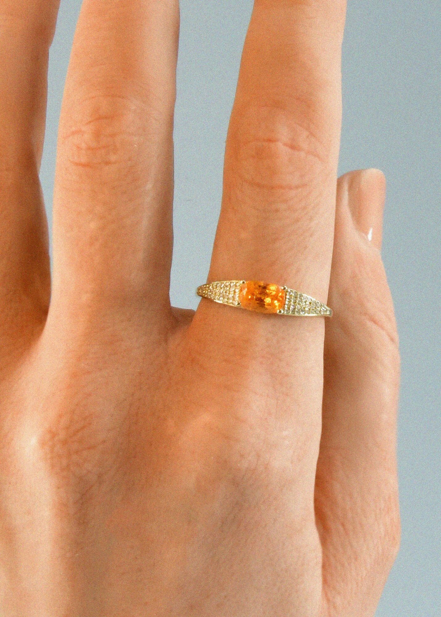 Close-up of a hand with a gold and orange ring on the ring finger.