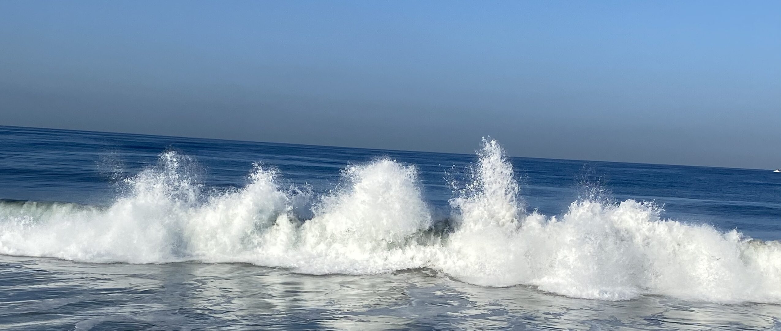 Waves crashing on the ocean with a clear blue sky above.