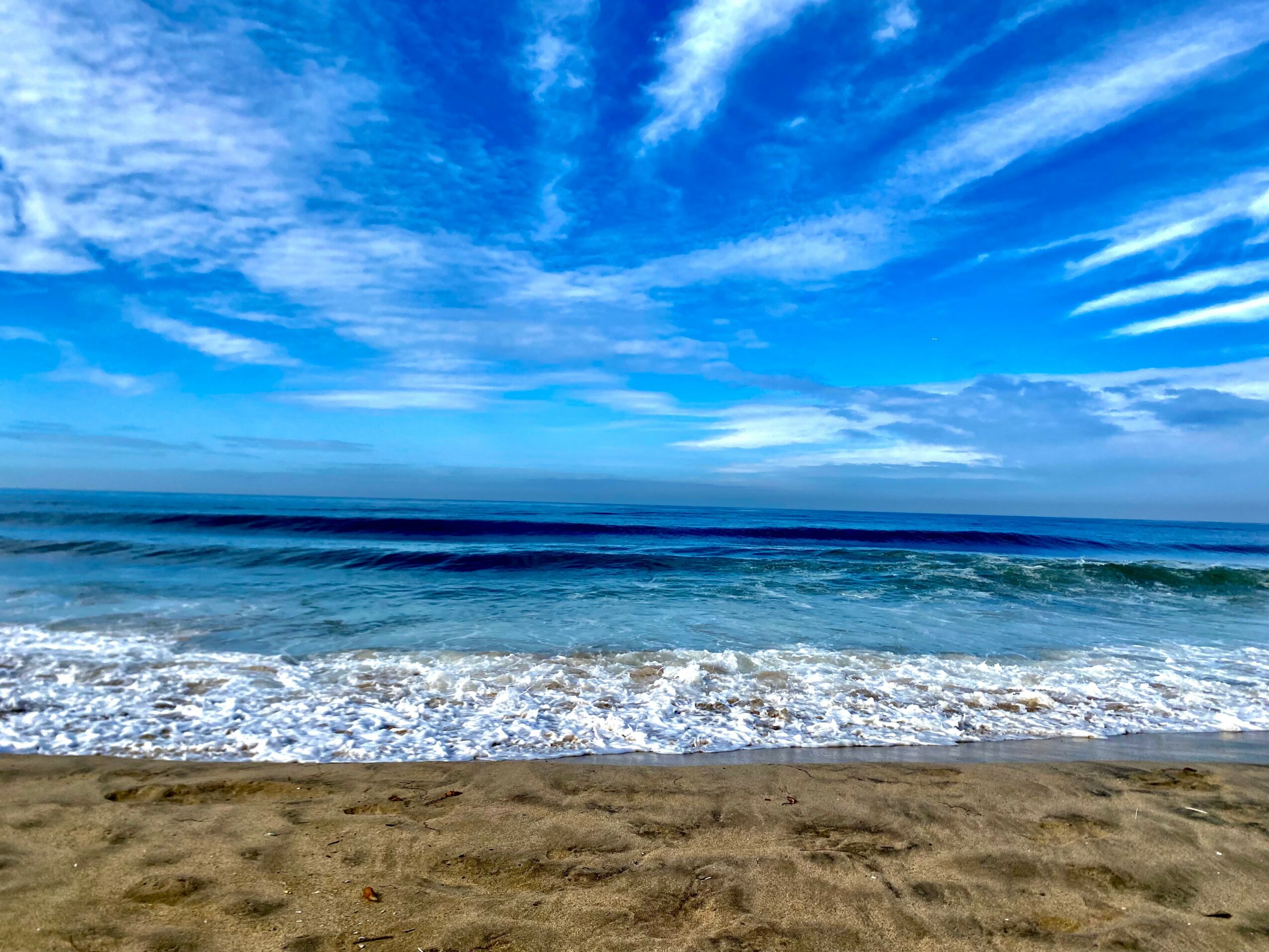 Beach with sandy shore, ocean waves, and blue sky with clouds.