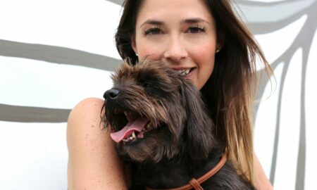 Woman smiling with a large, dark-colored dog in front of a white background with black lines.