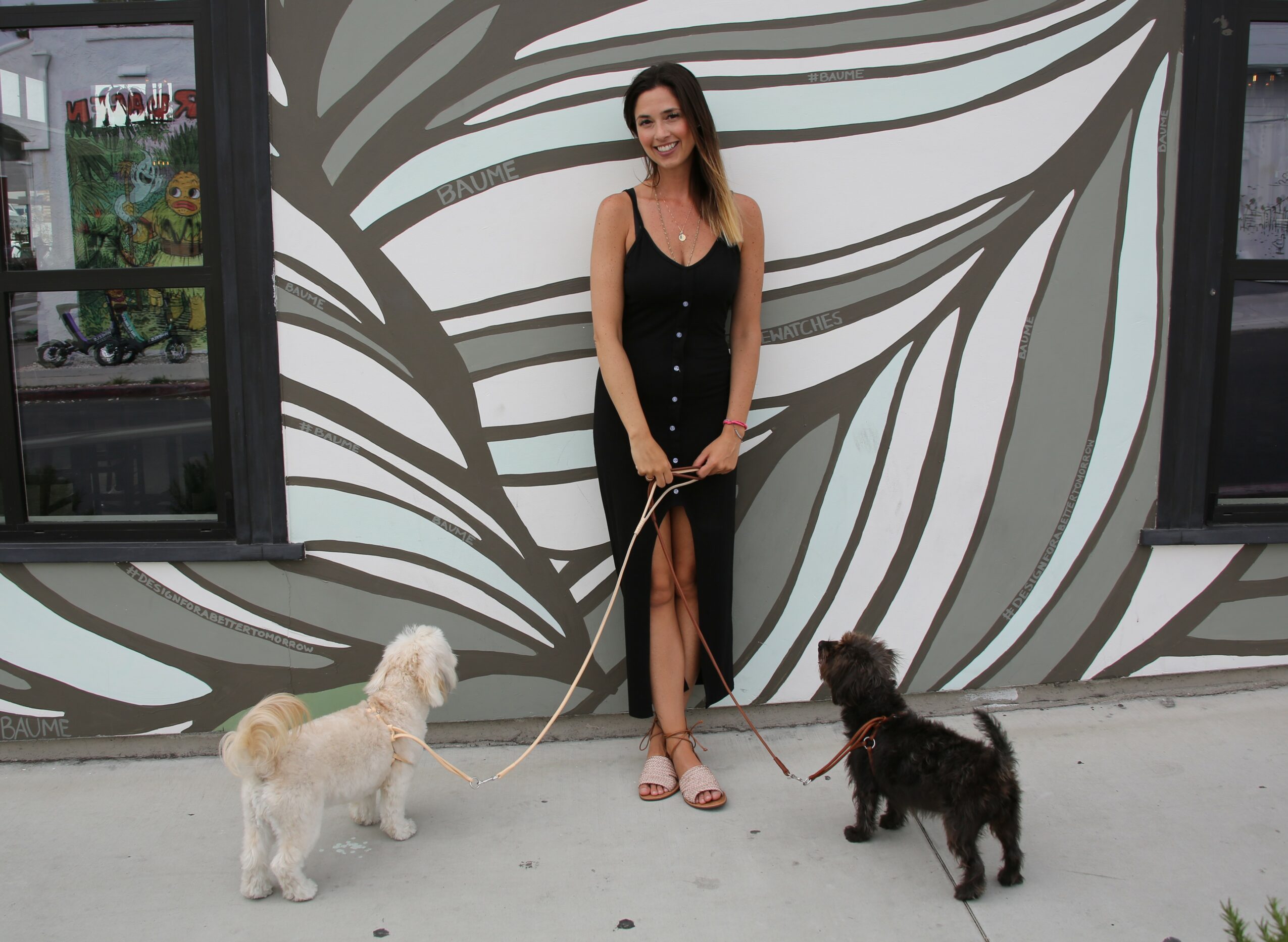 Woman in black dress holding two dogs on leashes in front of a patterned wall.