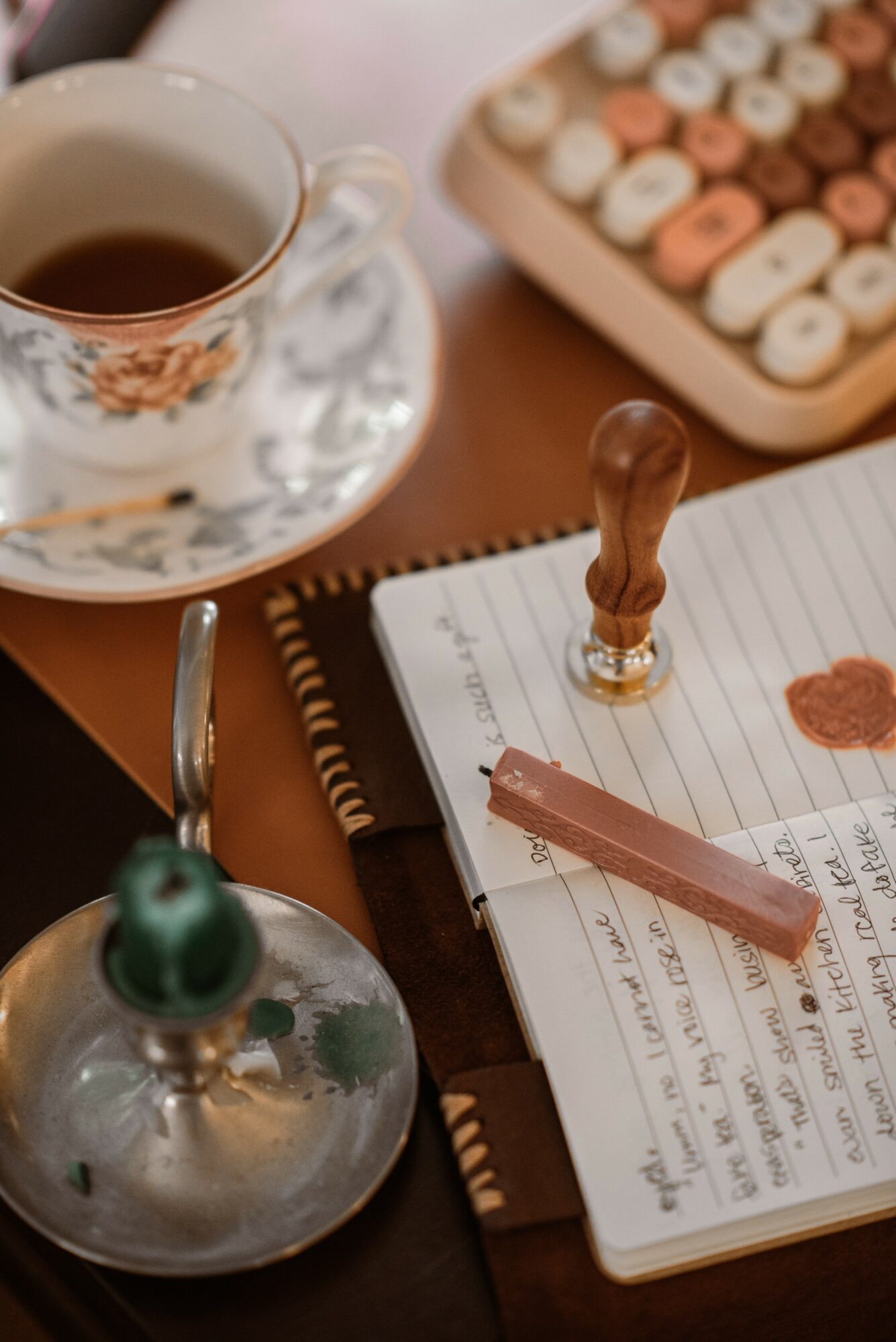 Cup of tea, notepad with a heart-shaped stamp, and a typewriter on a wooden table.
