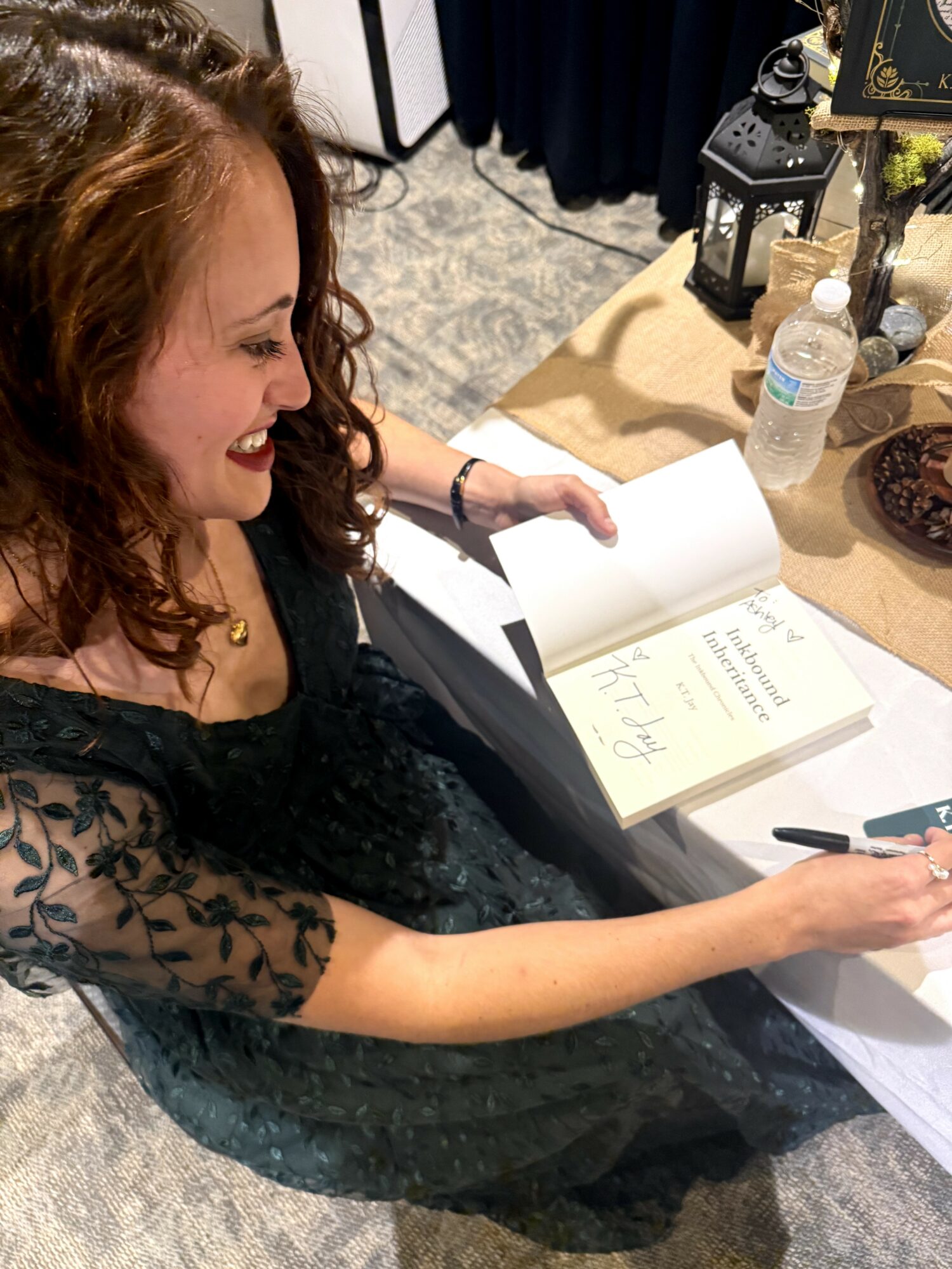 Woman with curly hair reading a book at a table with a pen in her hand, surrounded by water bottles and electronic equipment.