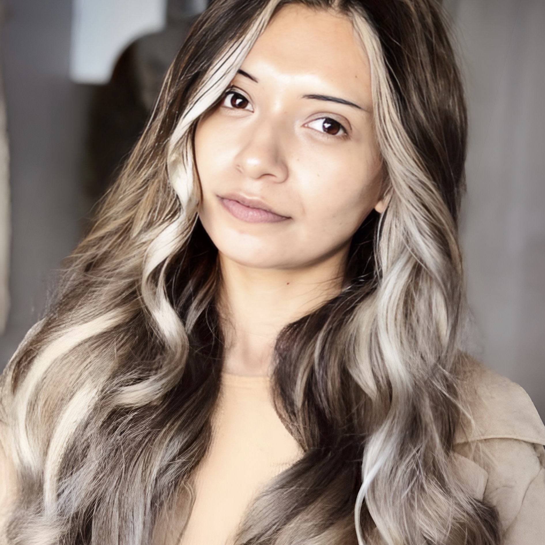 Young woman with long, wavy hair and light makeup, looking at camera with neutral expression.