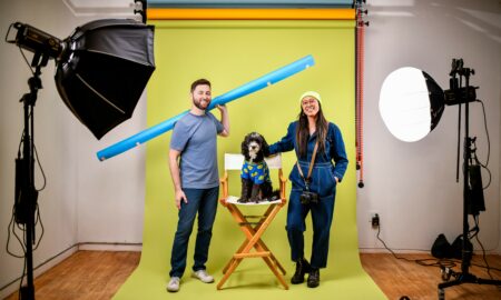 Two adults and a child with face paint in a photography studio with a yellow backdrop, surrounded by studio lights.