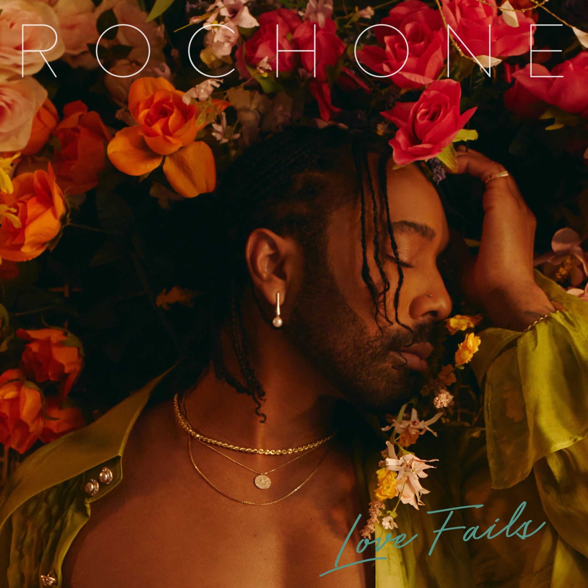 Person with closed eyes surrounded by colorful flowers, wearing earrings and layered necklaces, with hand near face.