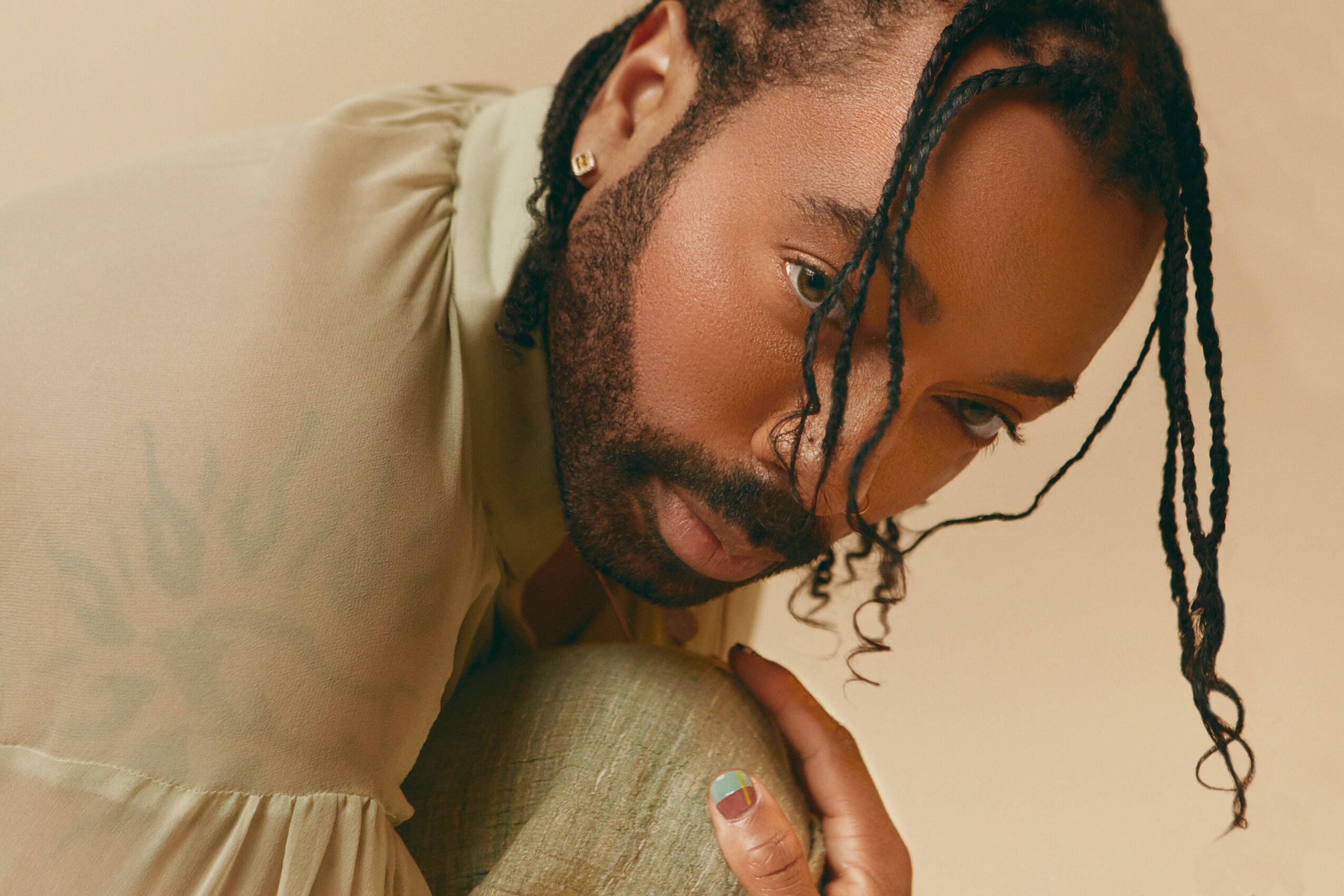 Close-up of a person with dreadlocks and a beard, looking downward, wearing a light-colored shirt.