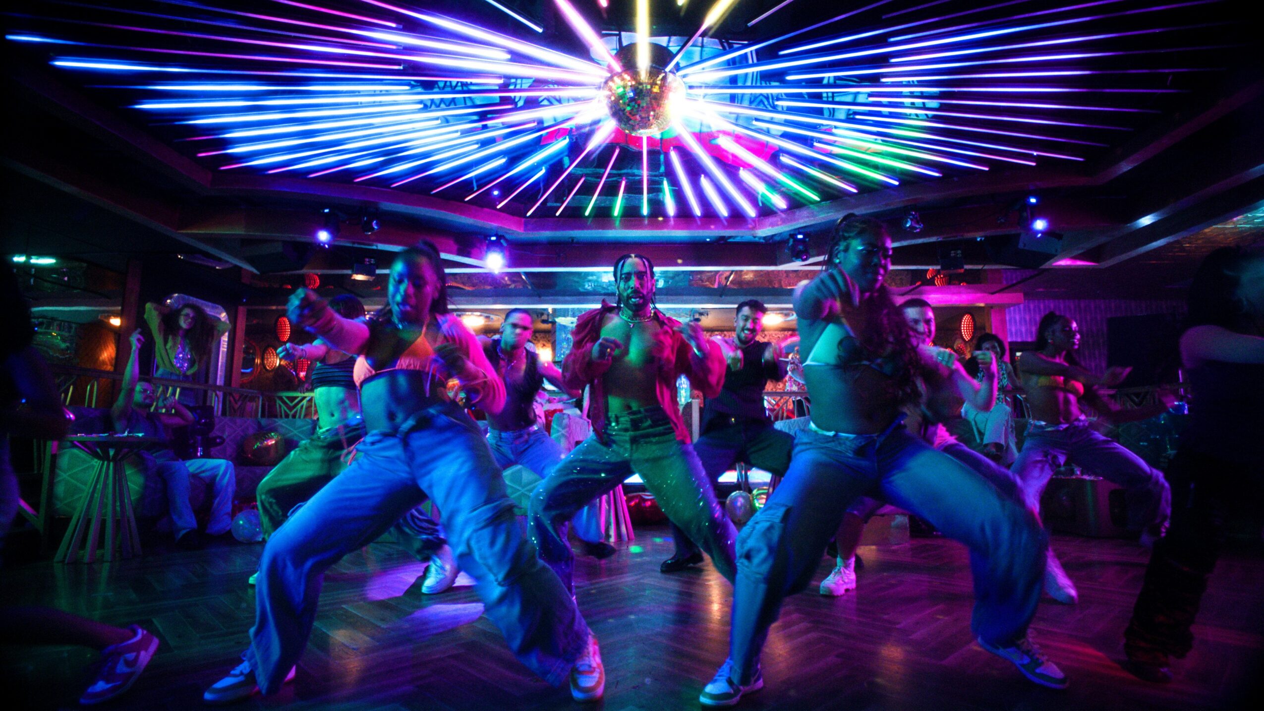 Group of people dancing under colorful, neon-lit ceiling in a lively nightclub.