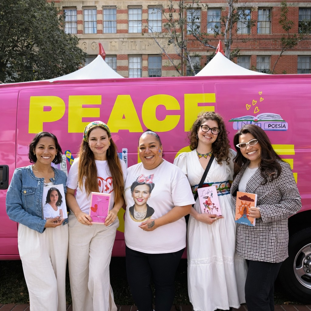 Five women standing outdoors in front of a pink banner with yellow text reading 'PEACE'. They hold books and photos, smiling.