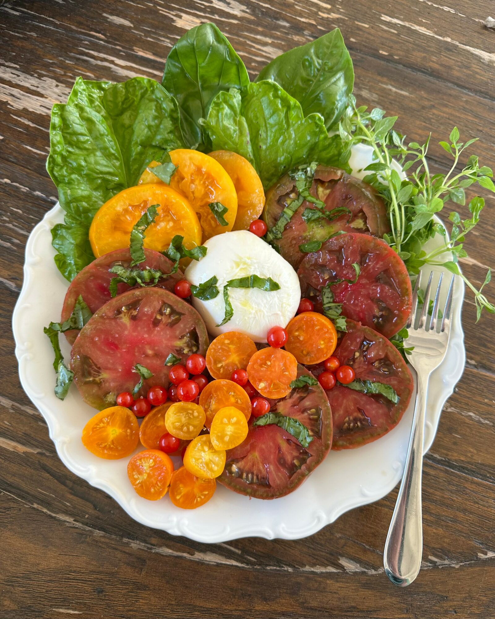 Salad with tomatoes, yellow cherry tomatoes, greens, a poached egg, and microgreens on a white plate.