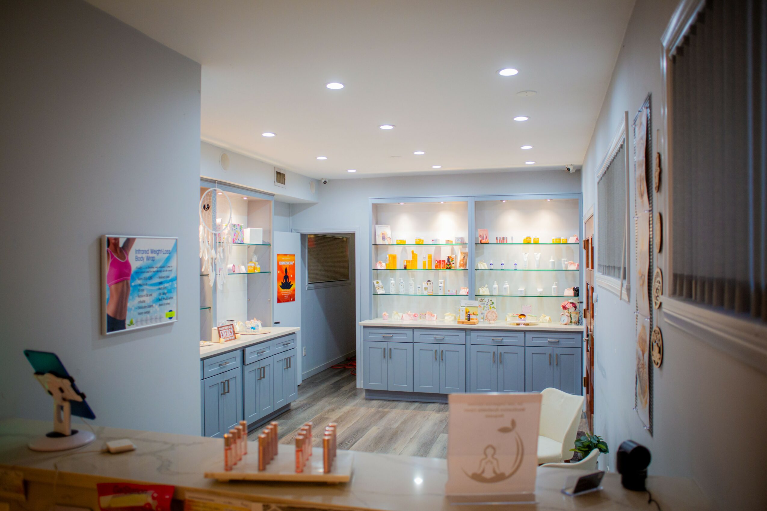 Room with blue cabinets, glass display shelves, artwork on walls, and a white chair near a window with blinds.