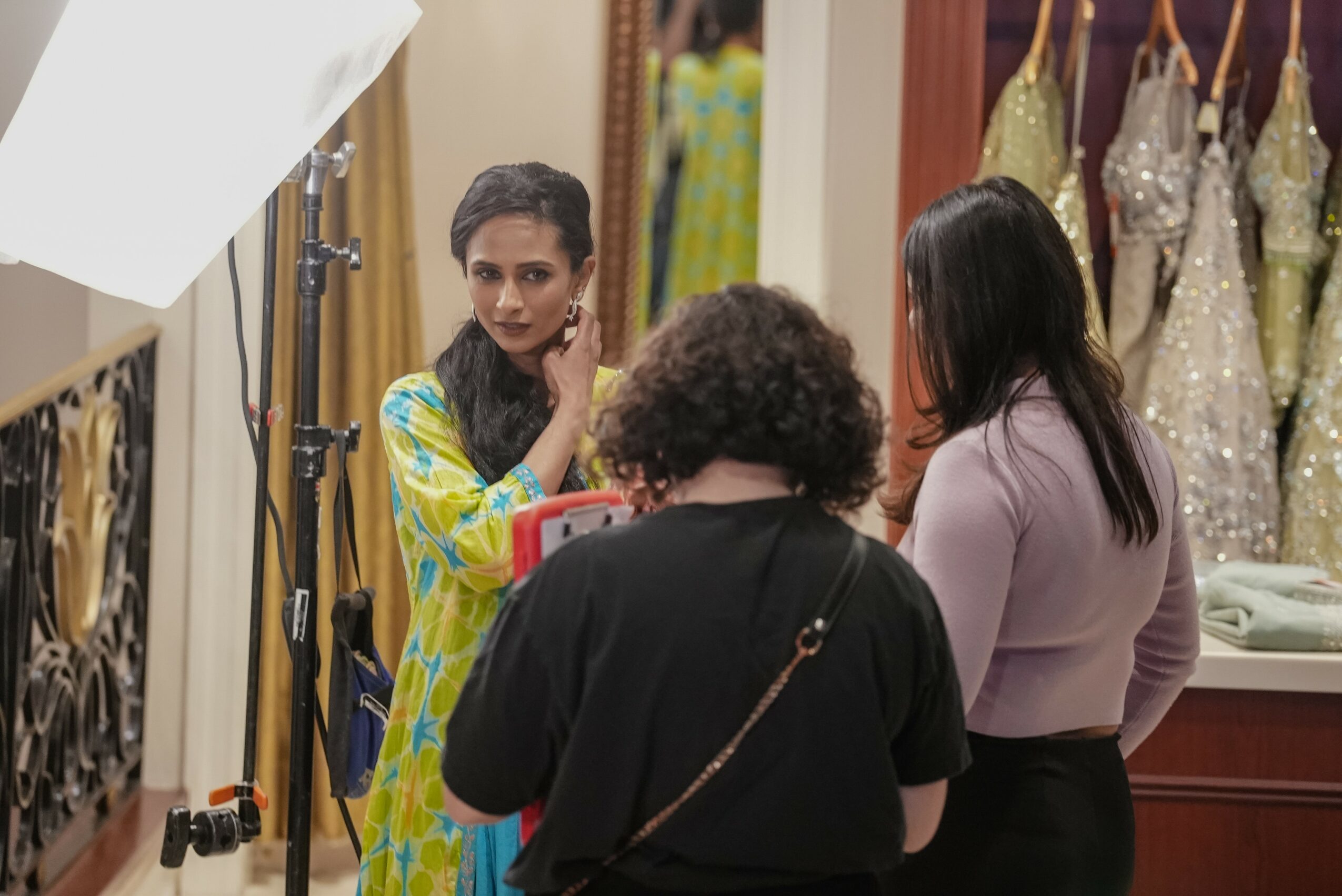 Three women in a clothing store engaged in conversation, with dresses displayed in the background.