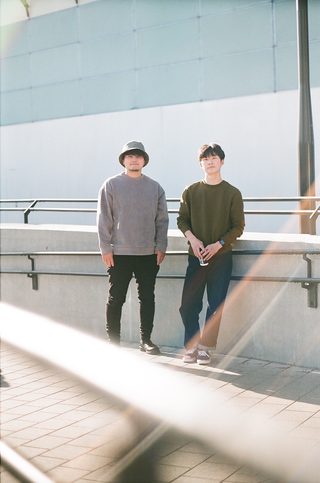 Two people standing outdoors near a railing, with a modern building in the background.