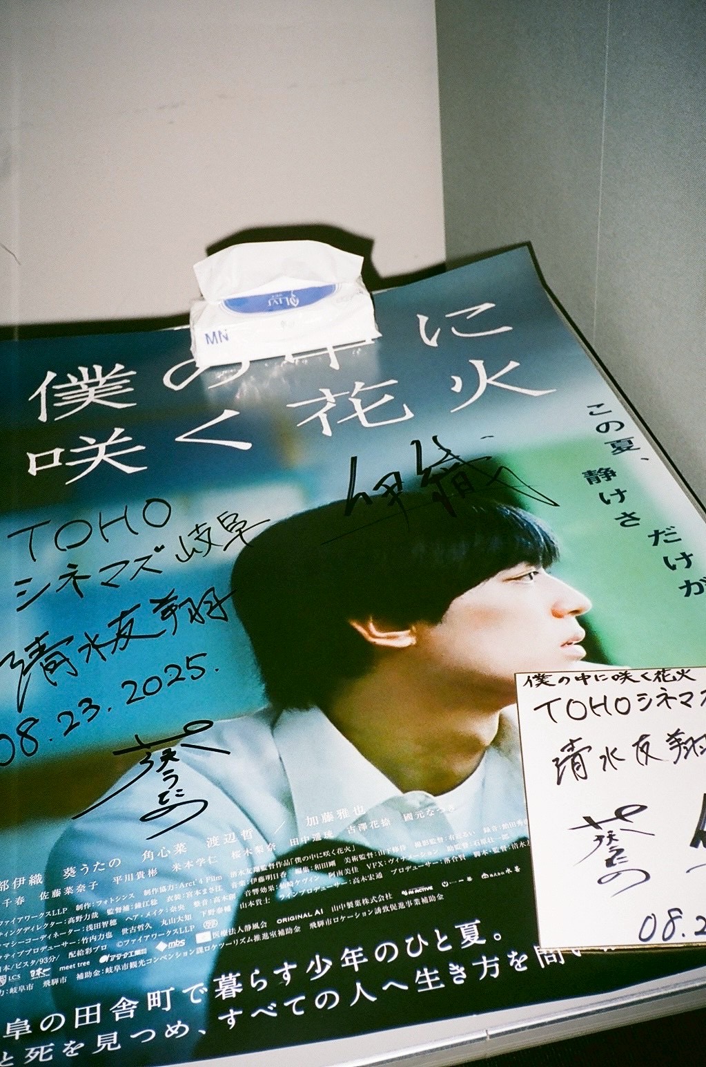 Person with short dark hair looking to the side, holding a paper, with a colorful background and a white object above.