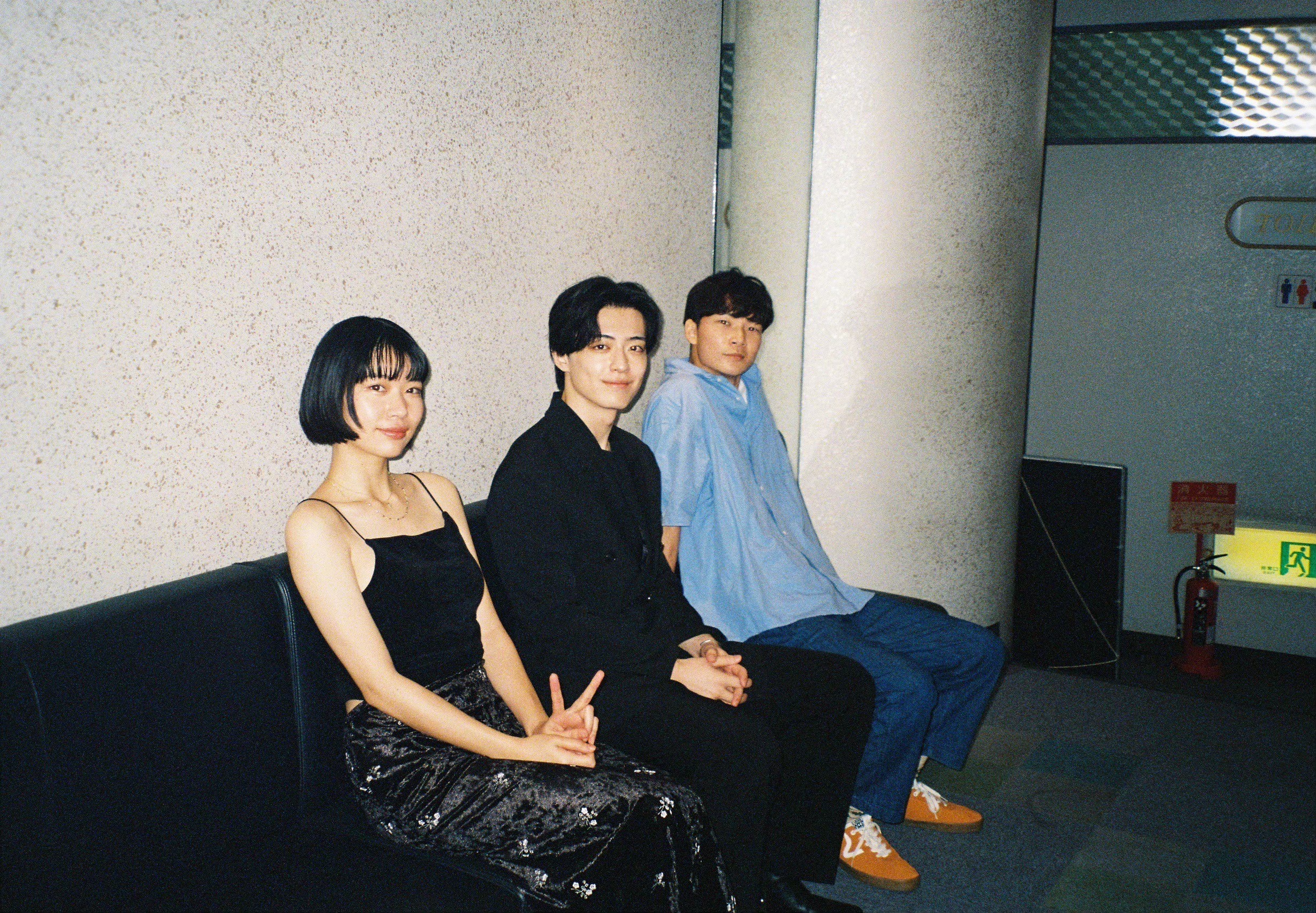 Three people sitting on a bench against a wall, two women and one man, in a dimly lit indoor setting.