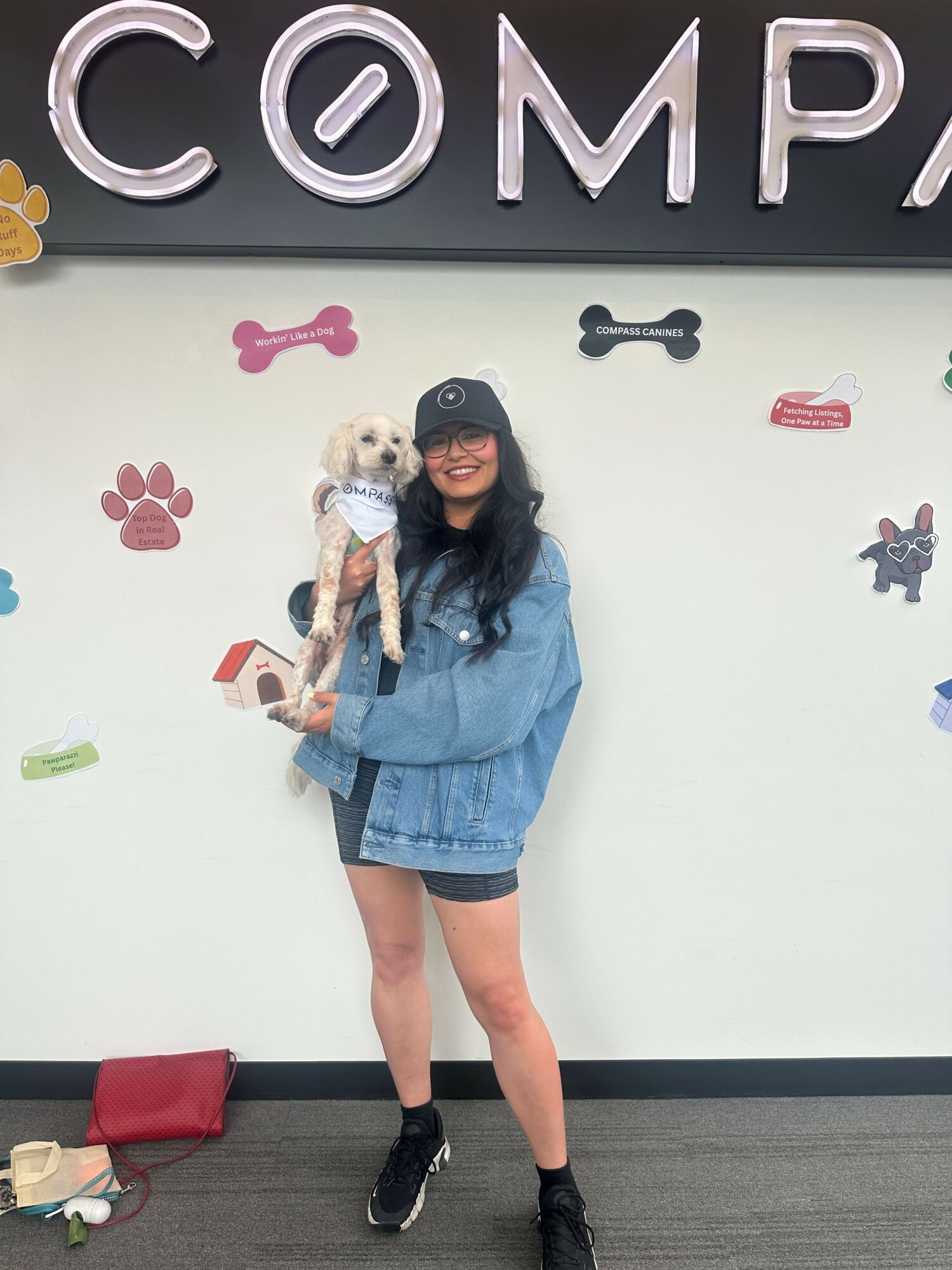 Person holding a small dog in front of a wall with dog-themed decorations and the word 'COMP'.
