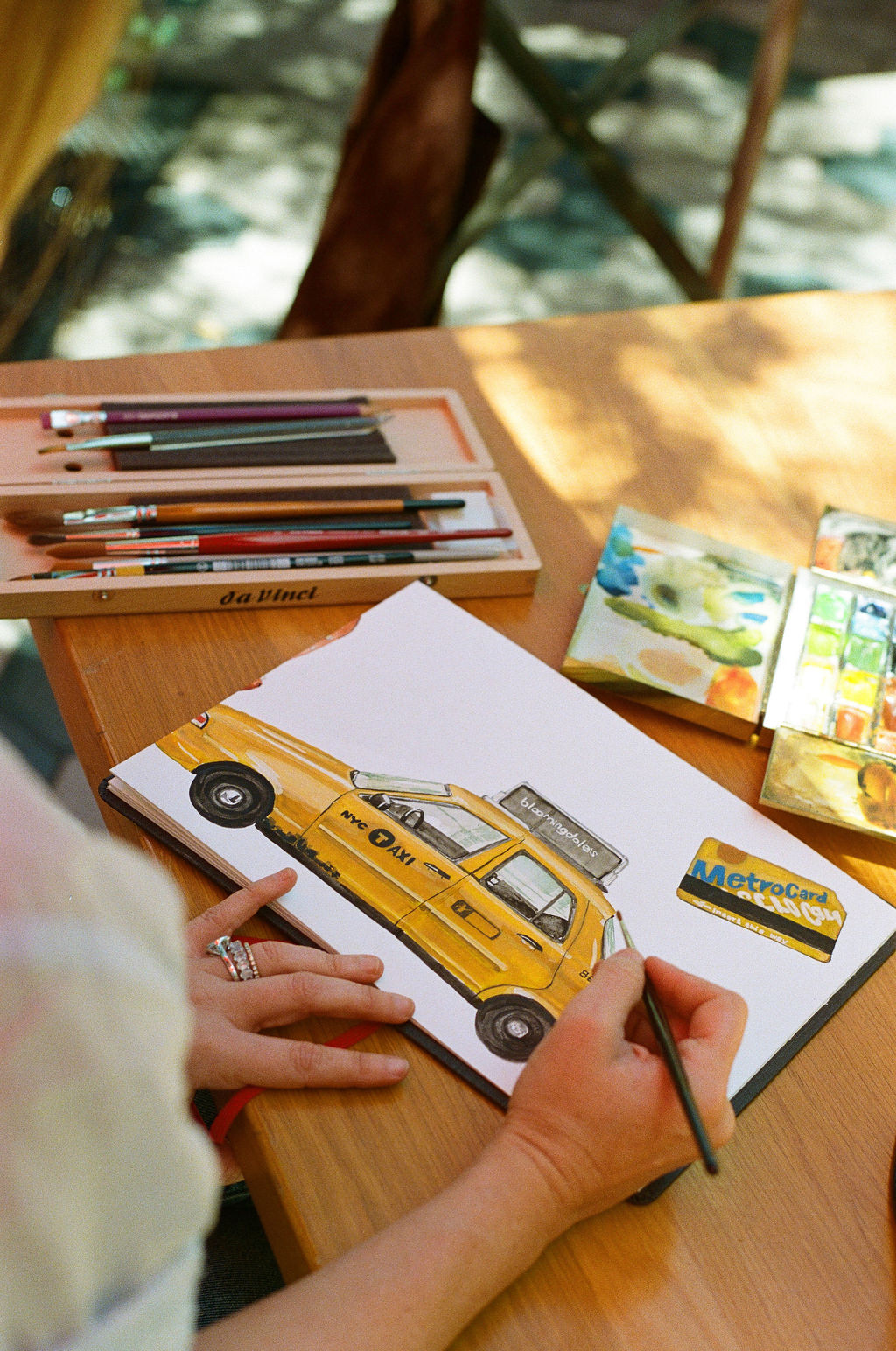 Child's hands drawing a yellow taxi on paper with colored pencils on a wooden table.