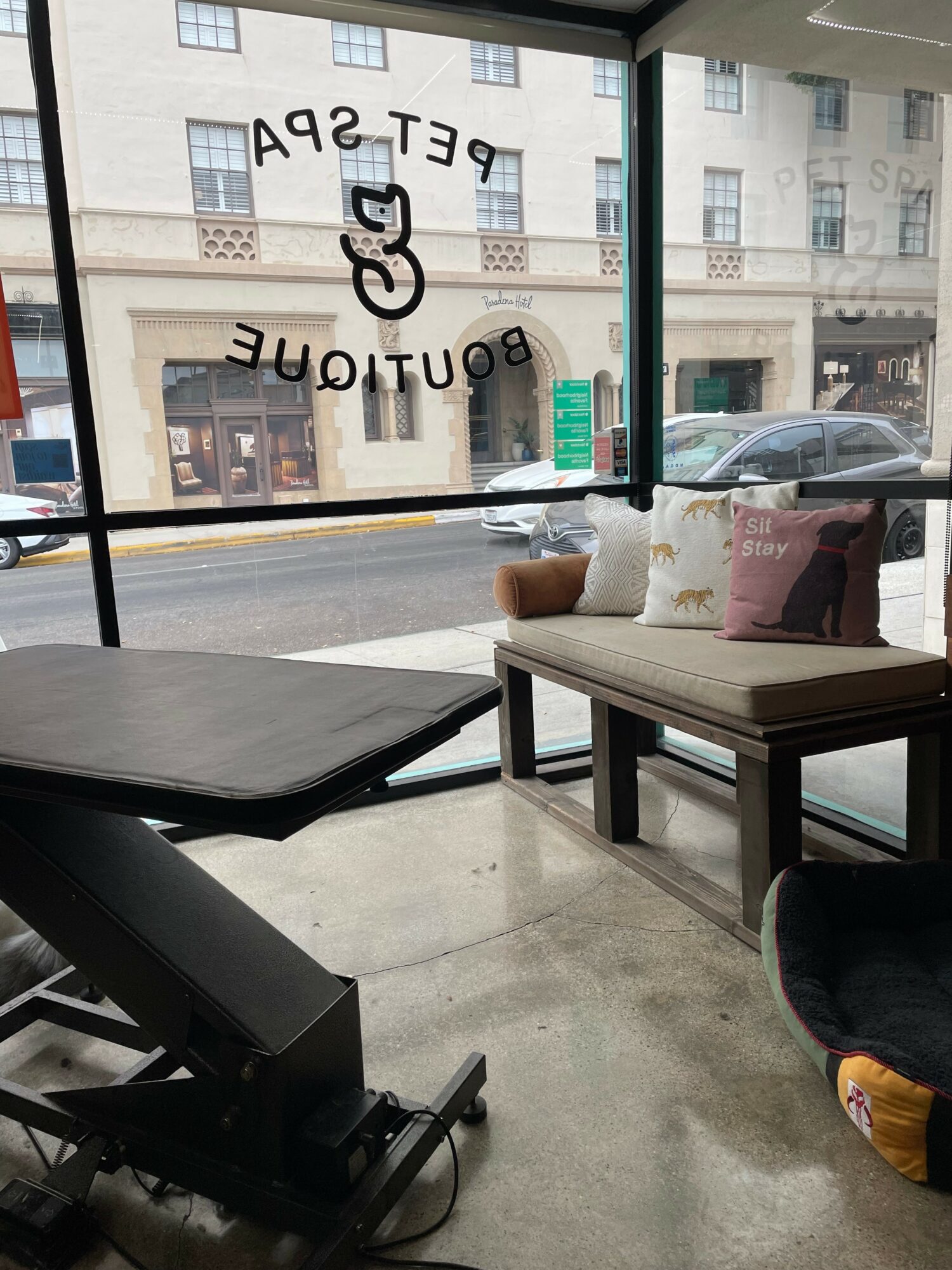 Interior view of a cafe with a window, seating area, and pillows, looking out onto a city street.