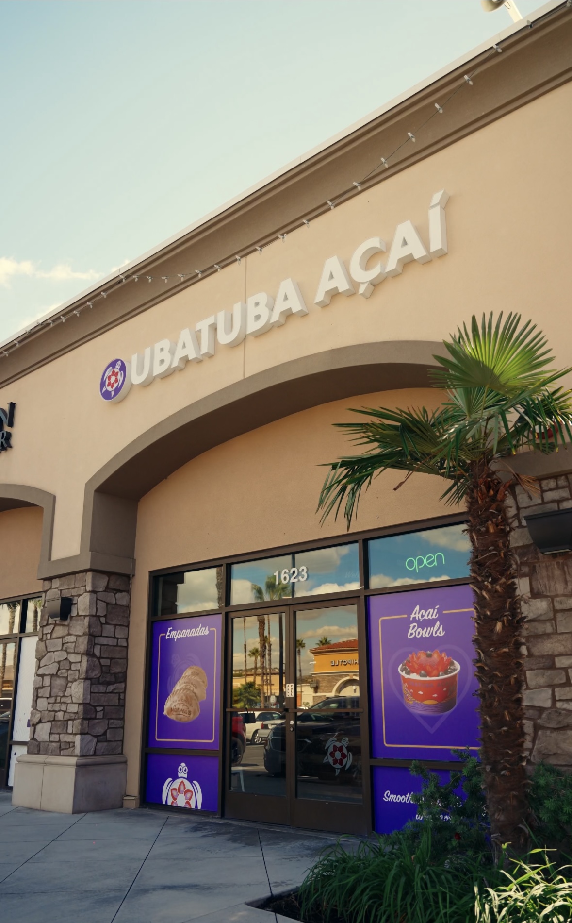 Store entrance with sign reading 'UBATUBA AÇAÍ', arched doorway, palm tree, and promotional posters outside.