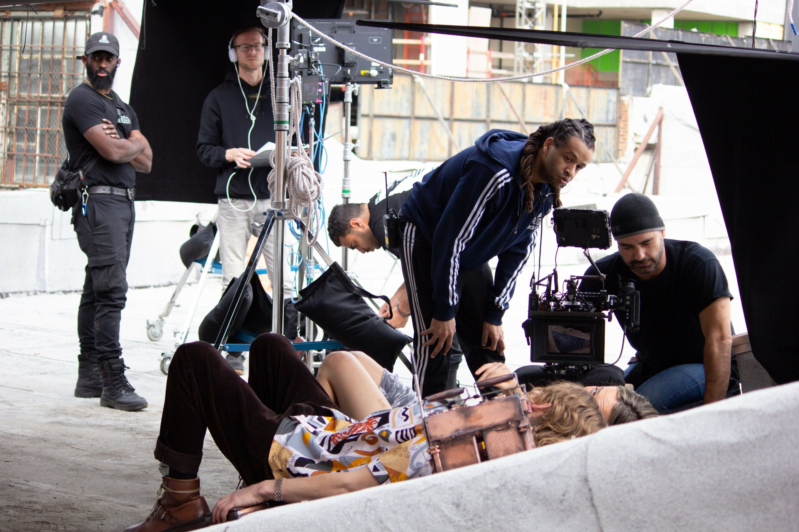People working on a photoshoot or film set with equipment and a person lying on the ground.