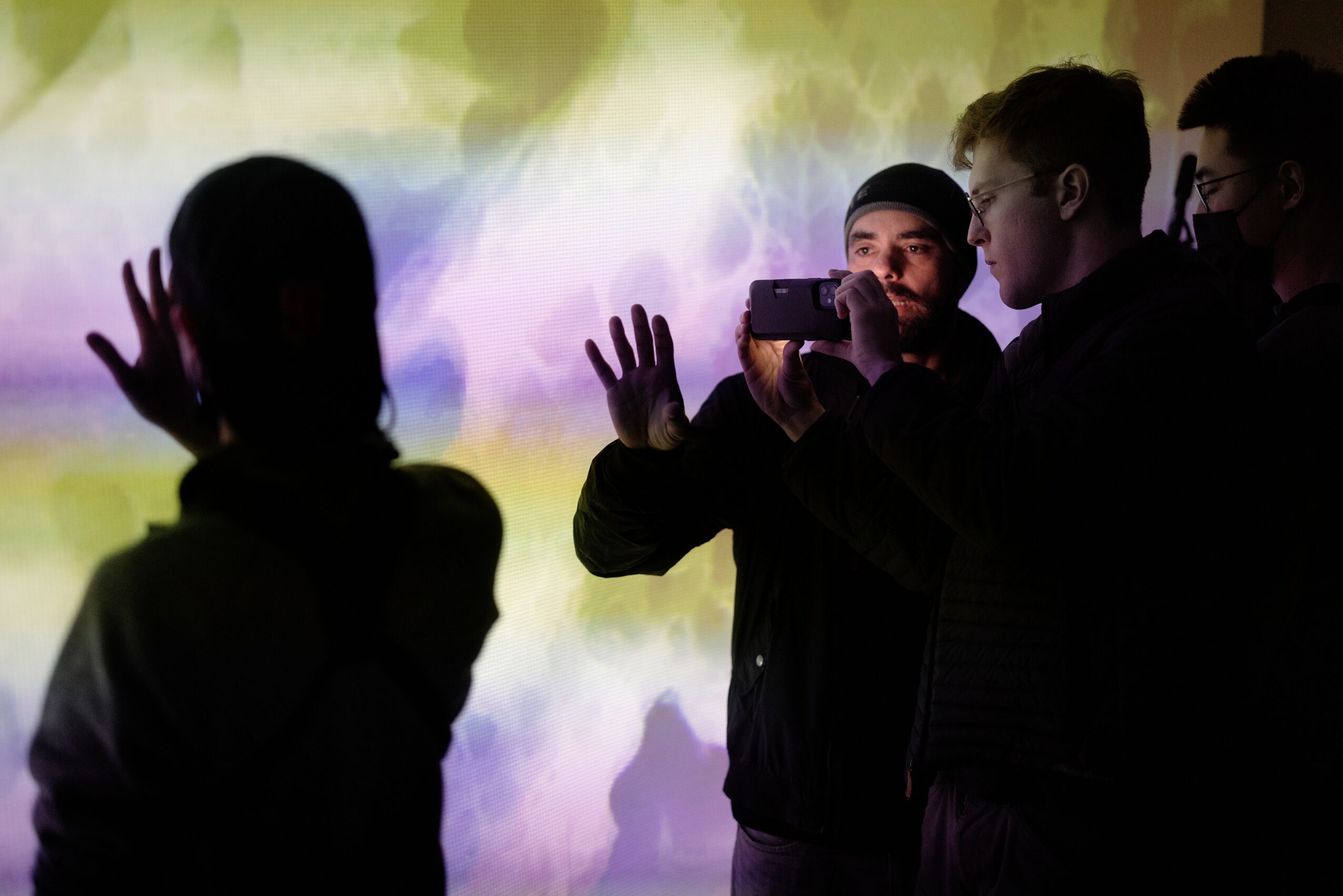 Group of people taking a photo of a person with hands raised against a colorful background.