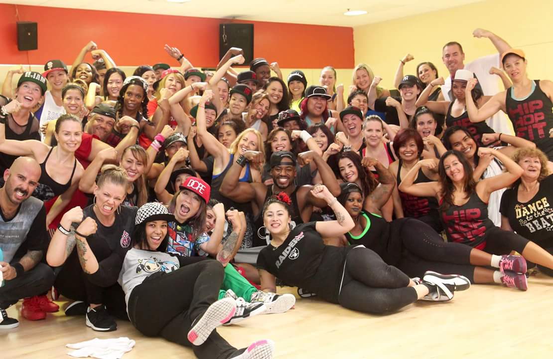 Group of diverse people in a dance studio, smiling and flexing muscles, celebrating together.