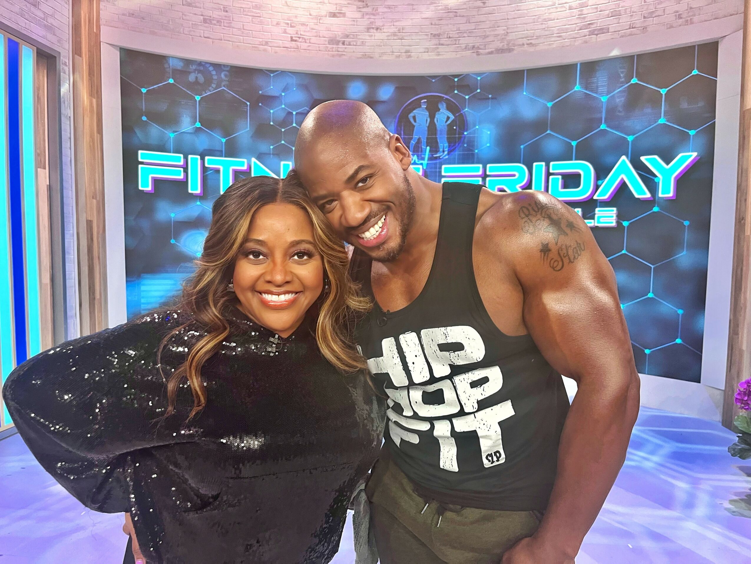 Two people smiling, standing close together in a fitness-themed studio with a digital background.