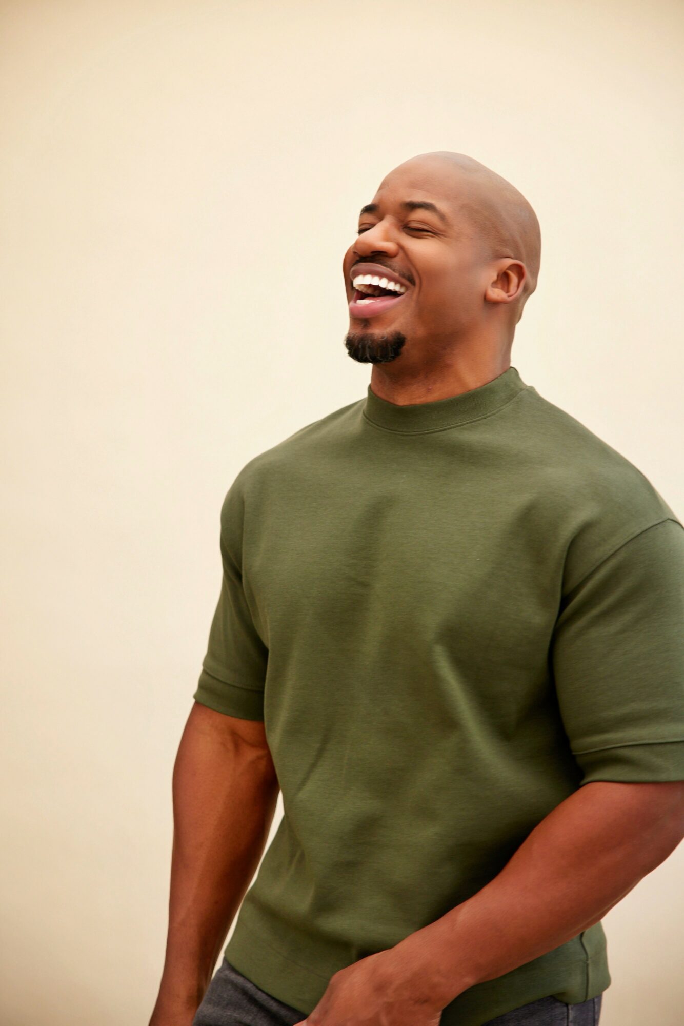 Smiling man with a beard and bald head wearing a green sweatshirt, standing against a plain background.
