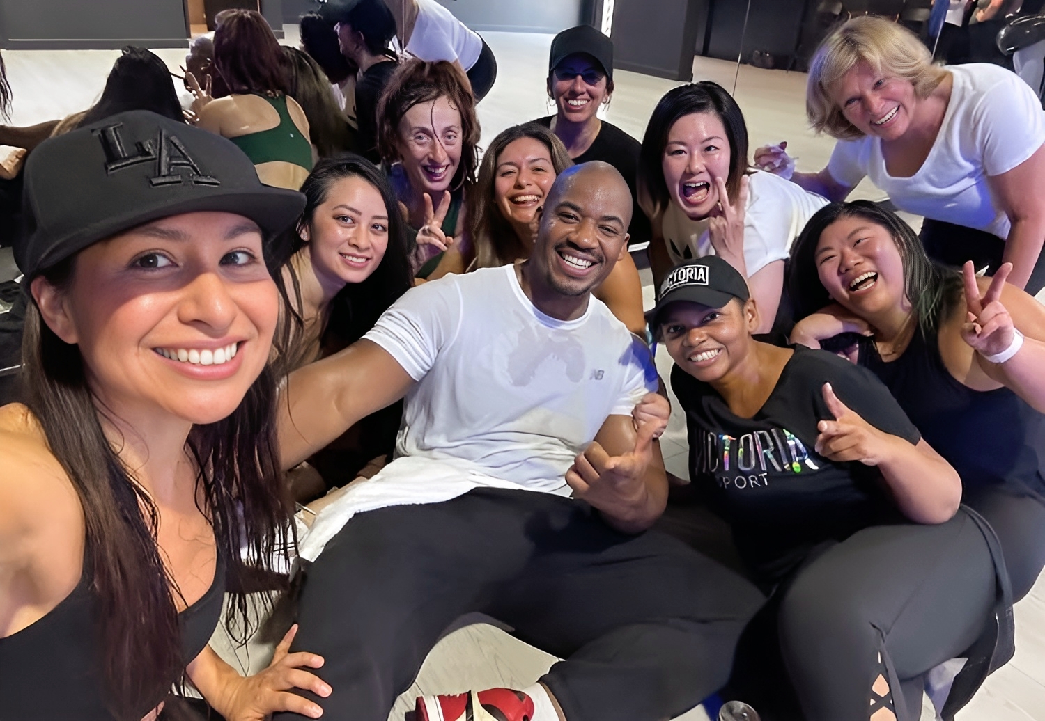 Group of smiling people, some making peace signs, gathered closely together indoors.