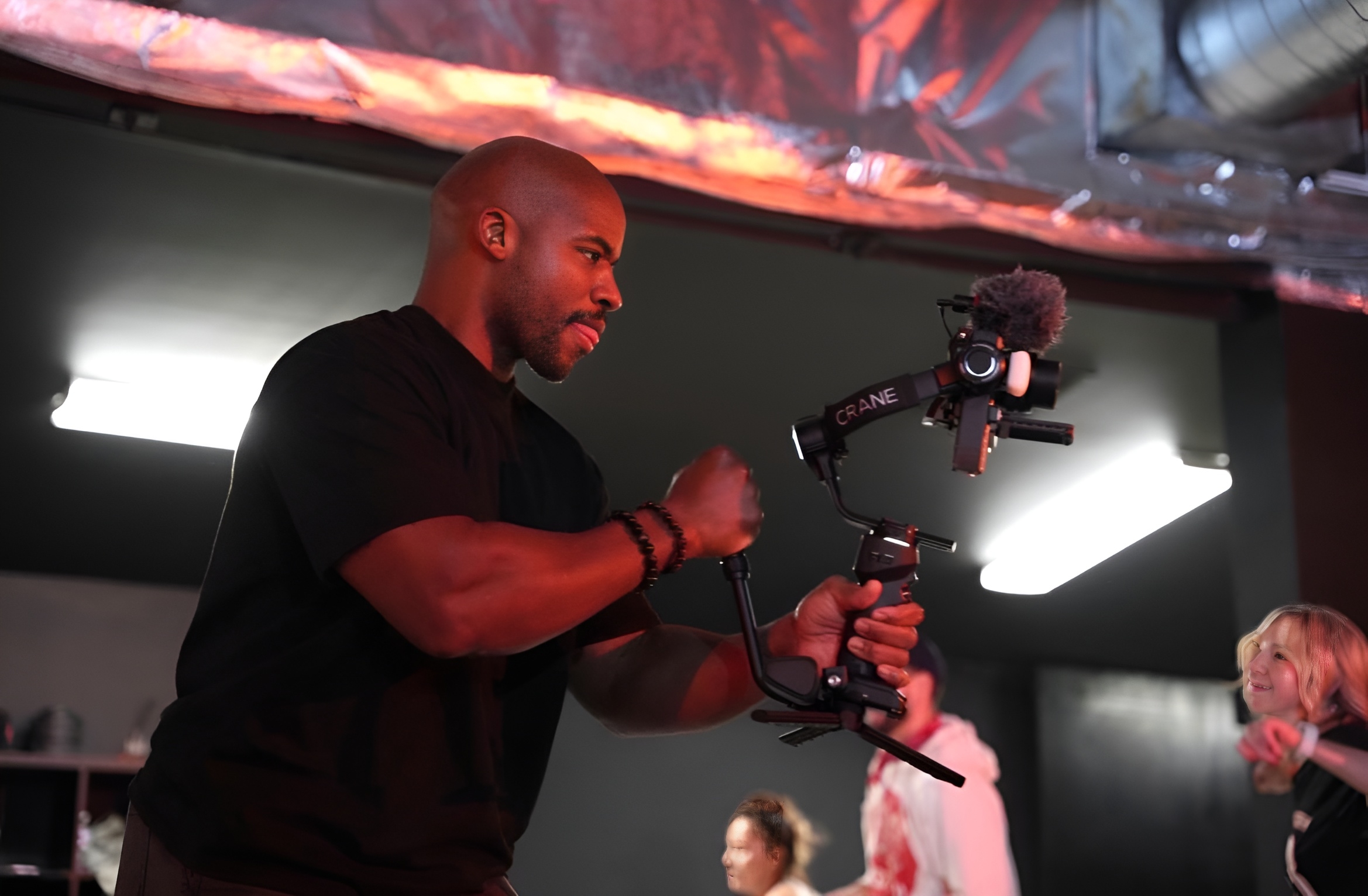 Man operating a camera with a stabilizer in a studio or event space, with people in the background.