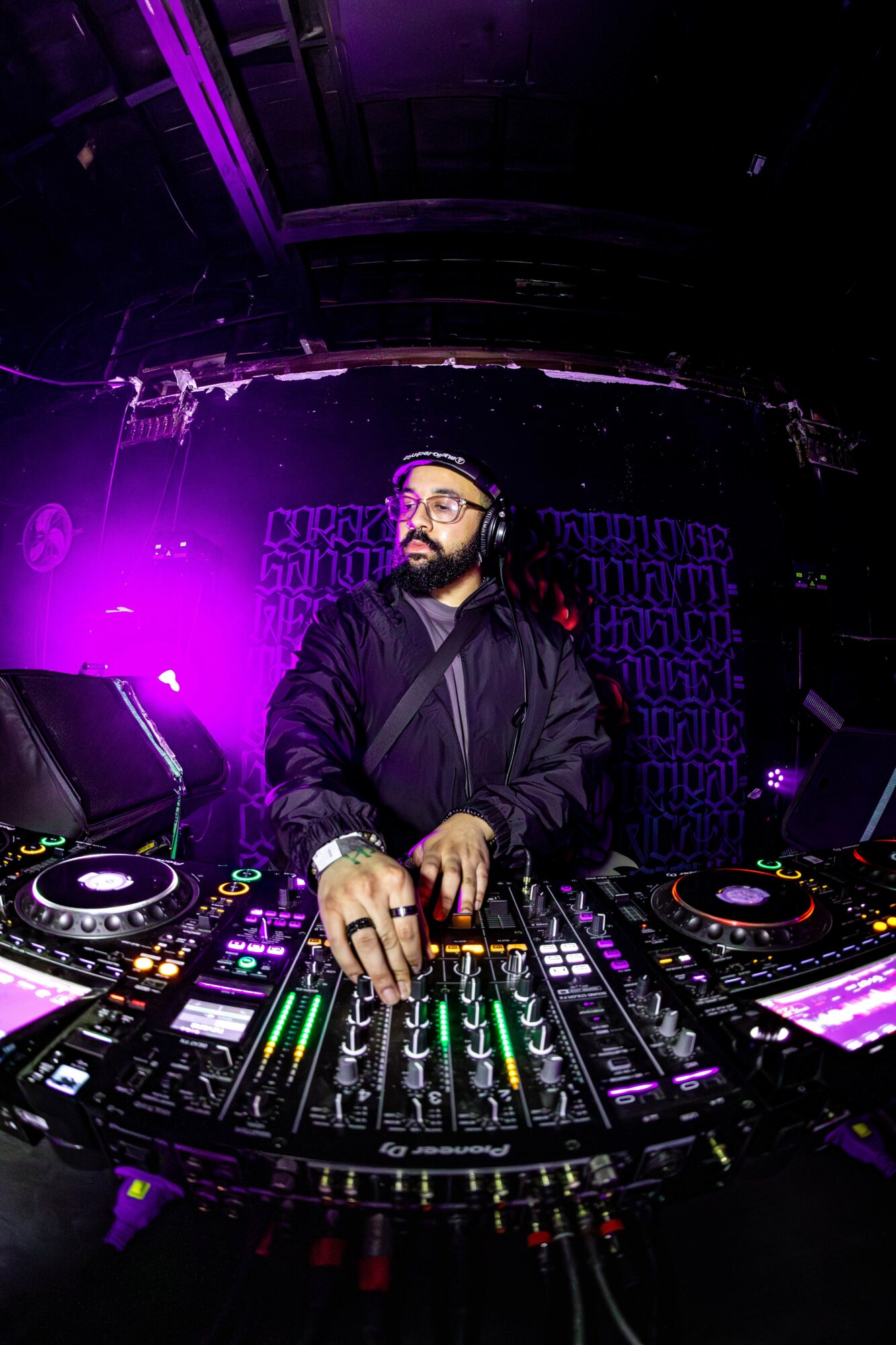 DJ with headphones operating turntables and mixer in a dark, purple-lit club setting.
