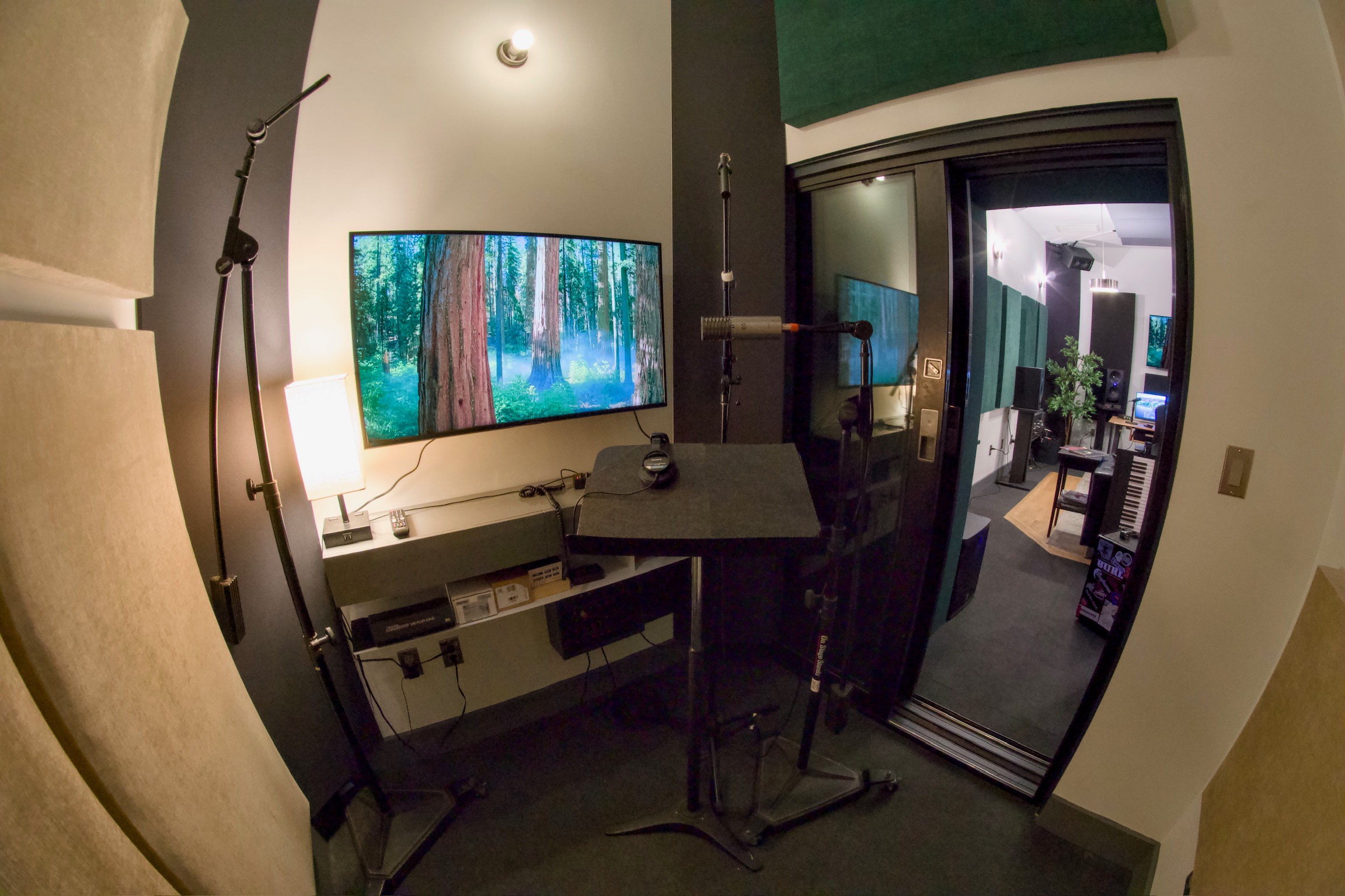 Room with a curved window, desk, monitor, and balcony door, viewed with fisheye lens distortion.