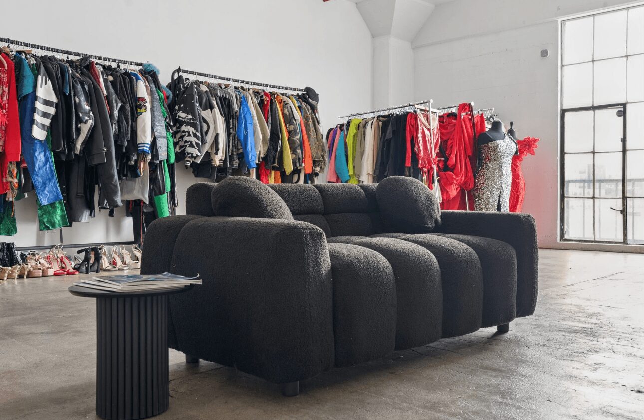 Black sofa with a small side table in a clothing store with racks of colorful clothes in the background.