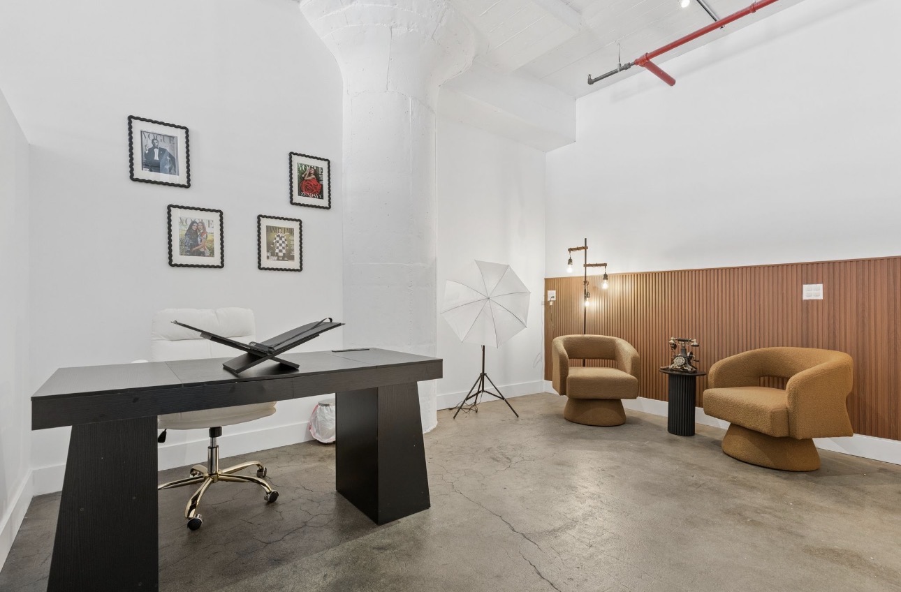Modern office space with a desk, chair, wall art, and seating area with two armchairs and a small table.