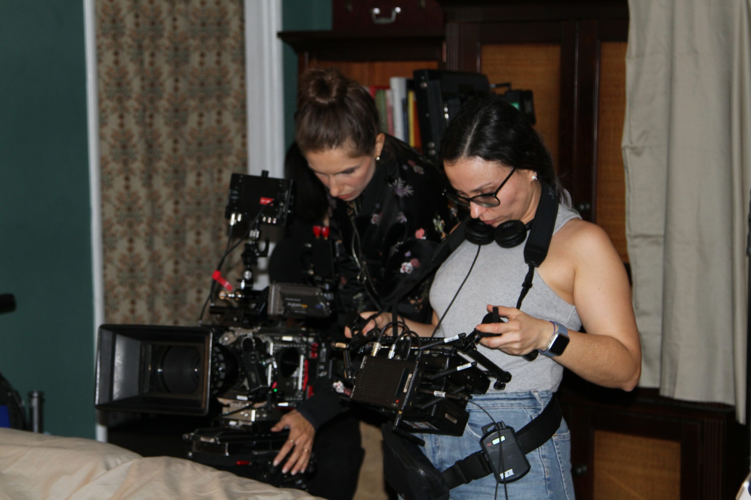 Two women working with professional camera equipment indoors, one adjusting settings, the other looking at a device.